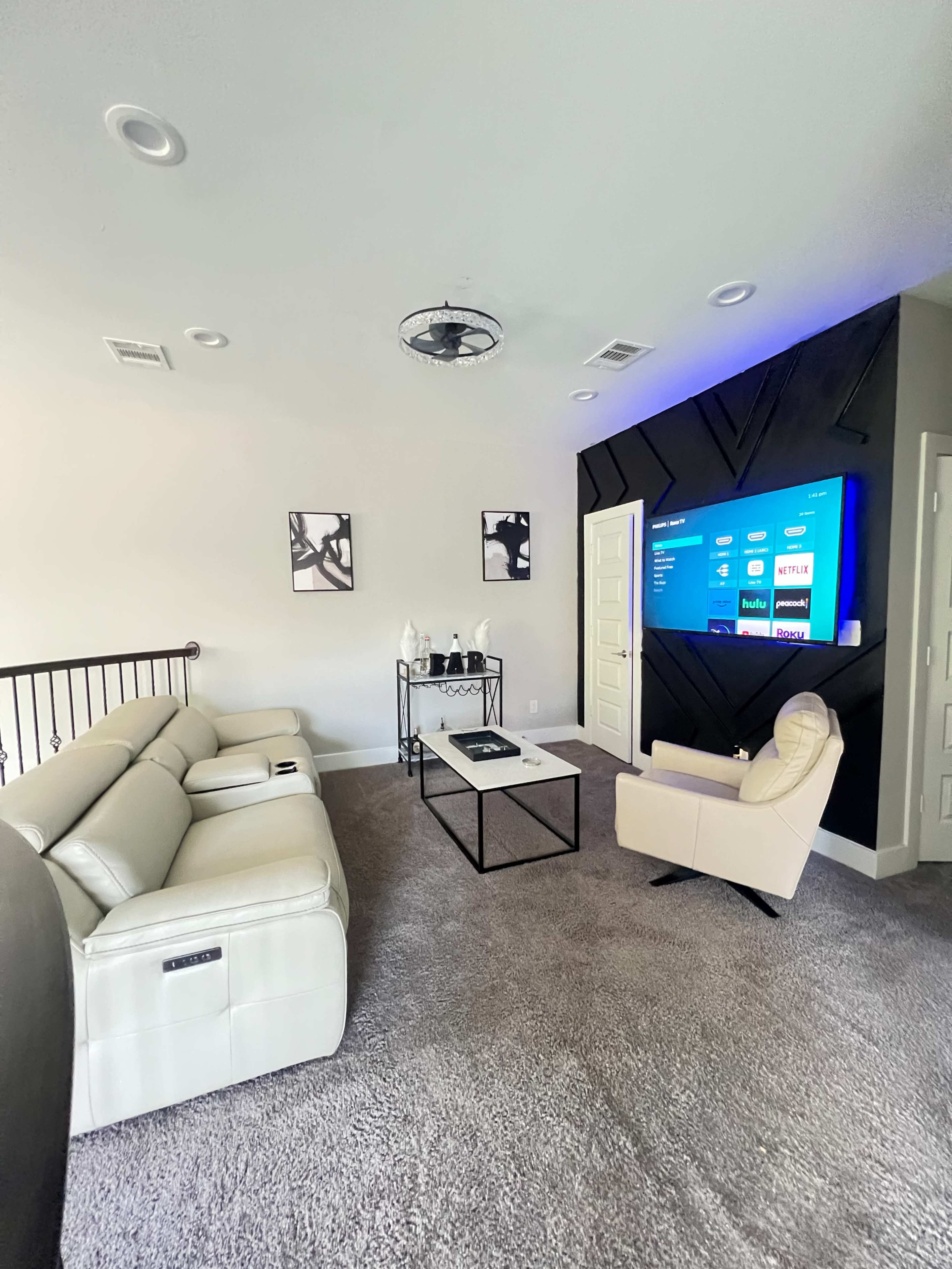 A modern living room with a light-colored sofa, a black coffee table, a television mounted on a textured wall, and decorative artwork.