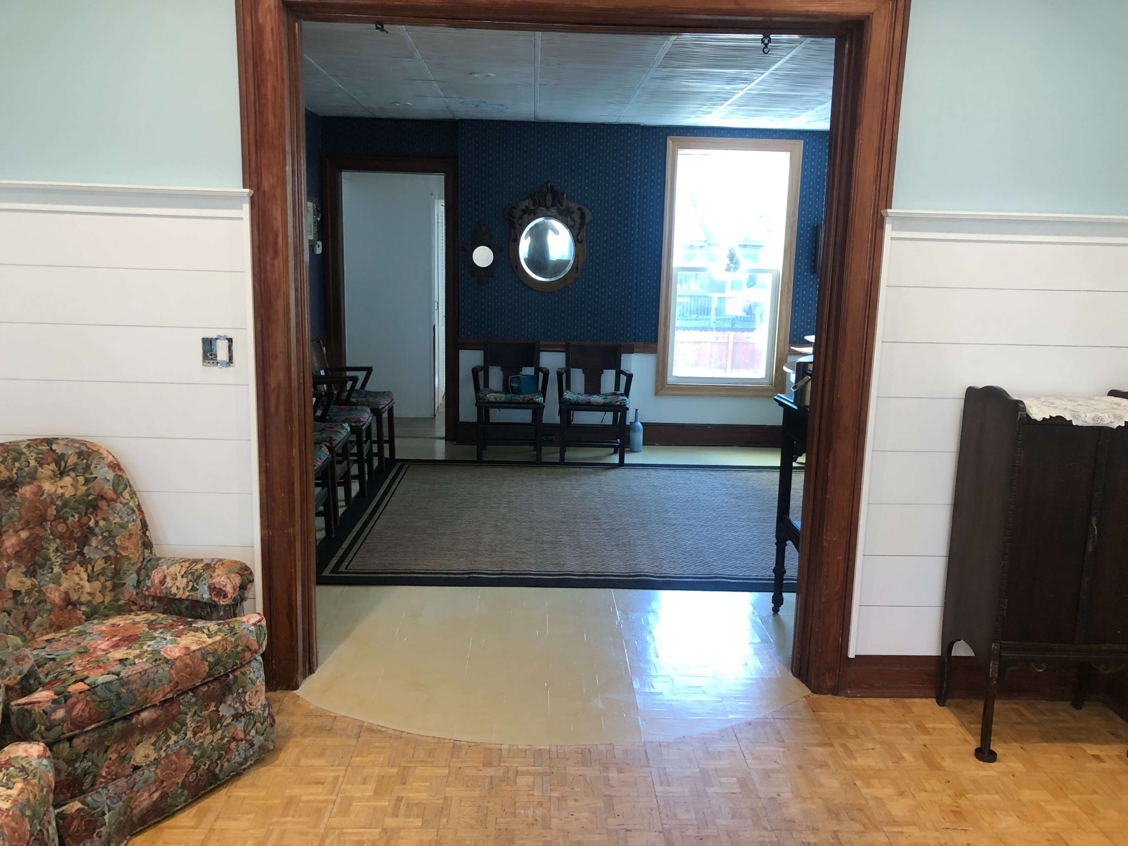 A floral couch is positioned in the foreground, leading to a room with a patterned carpet and a mirror on the opposite wall.