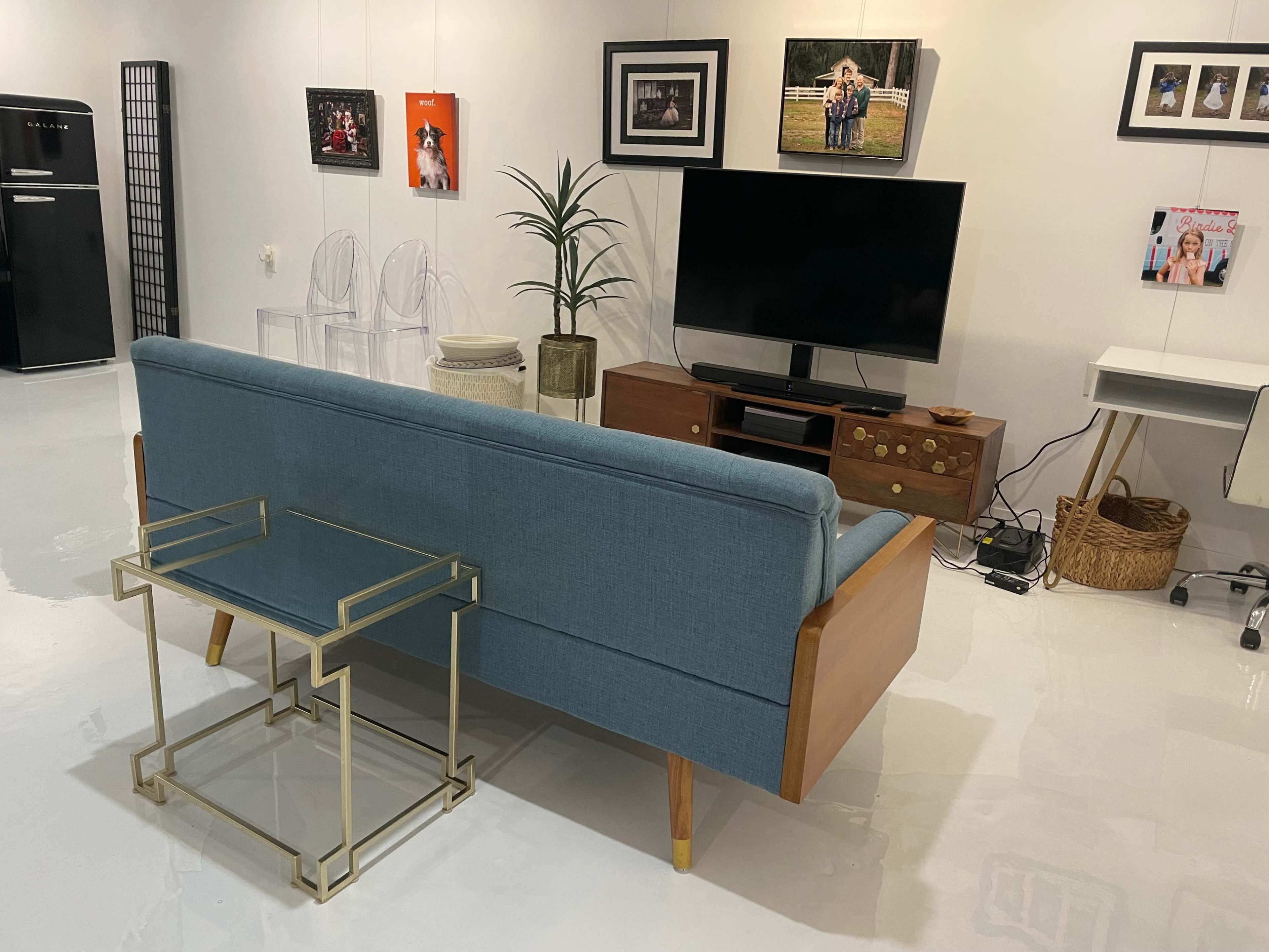 A modern living space features a blue upholstered sofa facing a television, accompanied by a metal side table and framed photos on the walls.