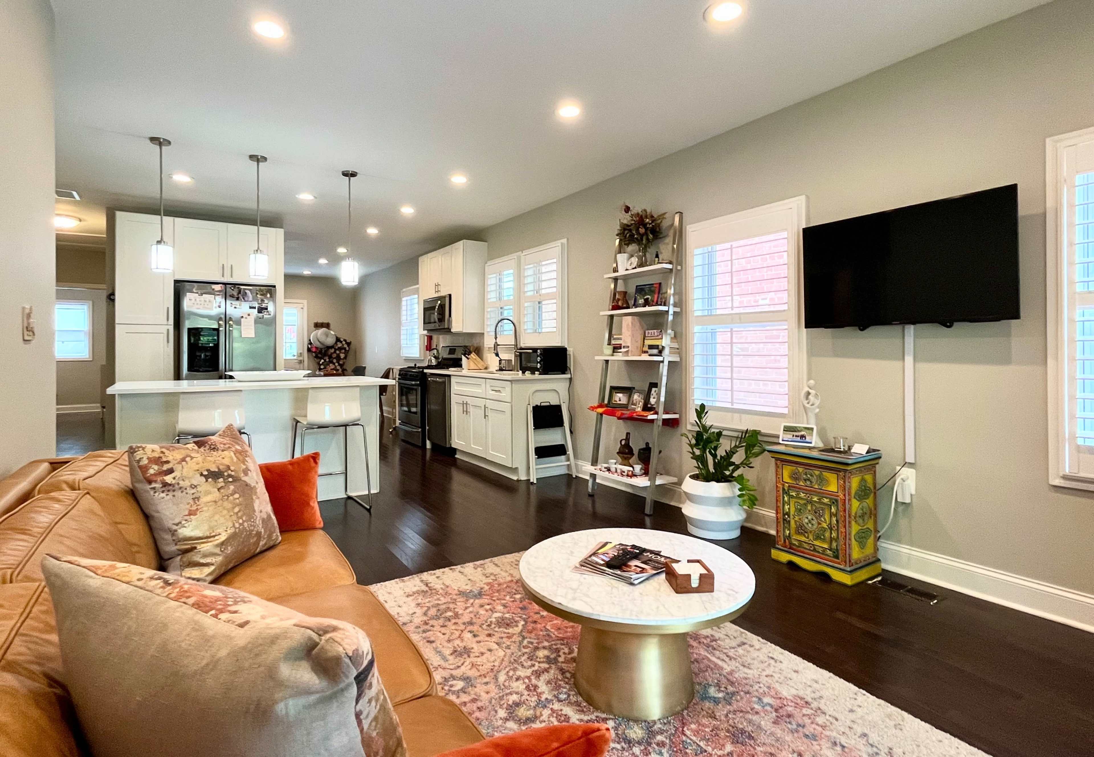 A well-lit living area showcases a modern kitchen with bar seating, a comfortable sofa, and a decorative coffee table.