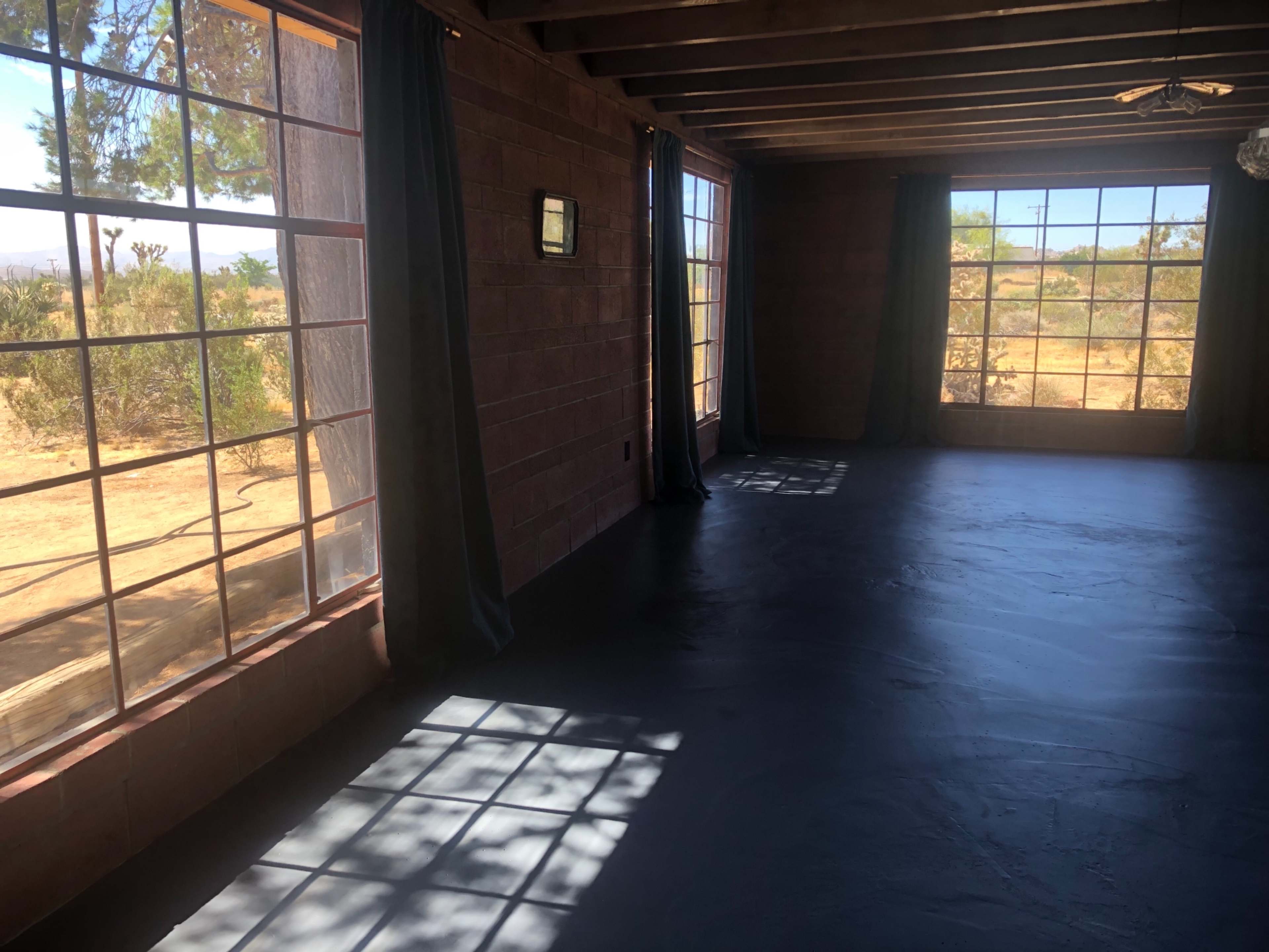 An empty room with large windows, allowing natural light to stream in and illuminating the concrete floor.