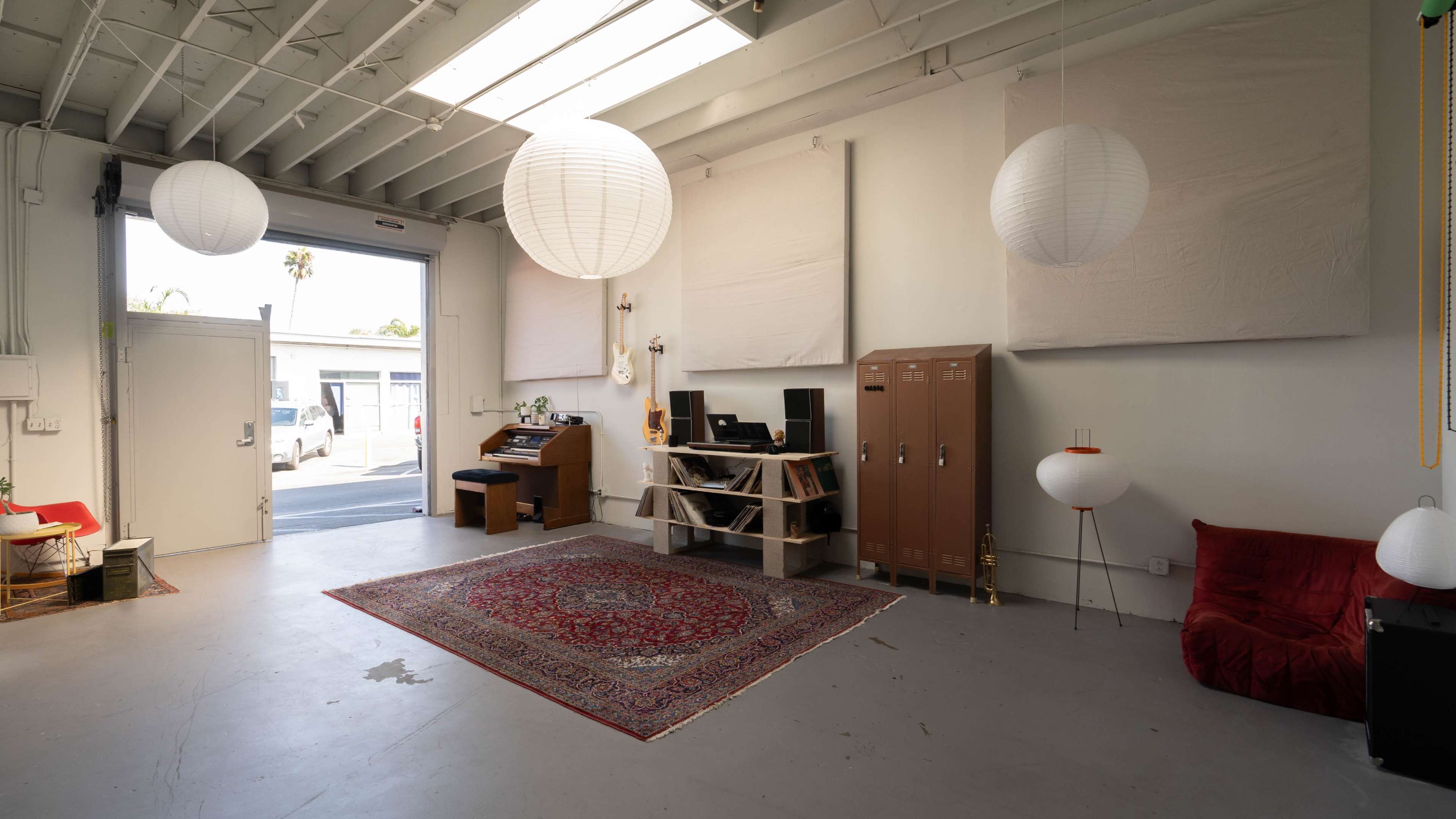 A well-lit studio space with a red rug, a wooden desk with a computer, filing cabinets, and hanging paper lanterns.