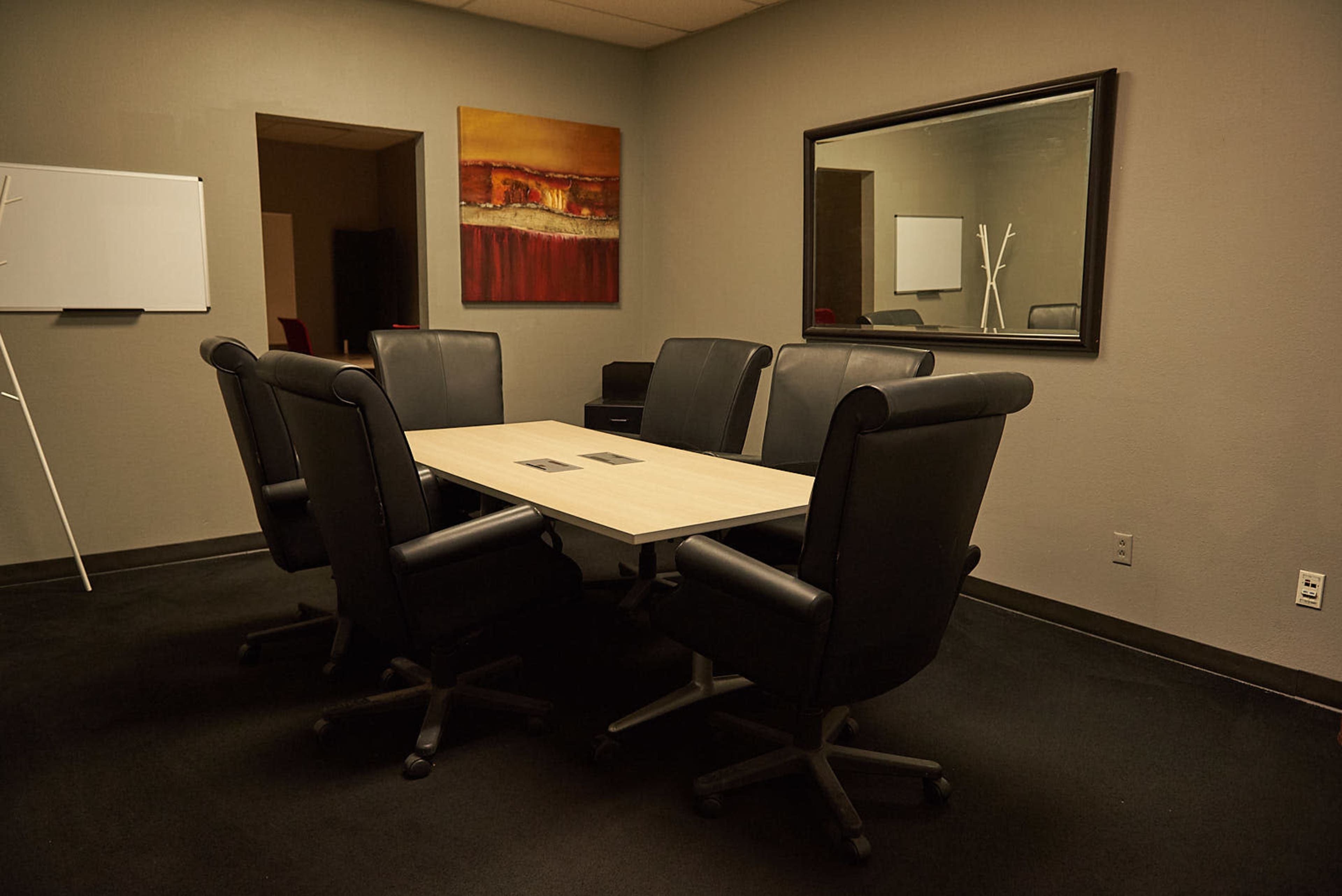 A conference room with a rectangular table surrounded by six black leather chairs, and a mirror reflecting the room's decor.