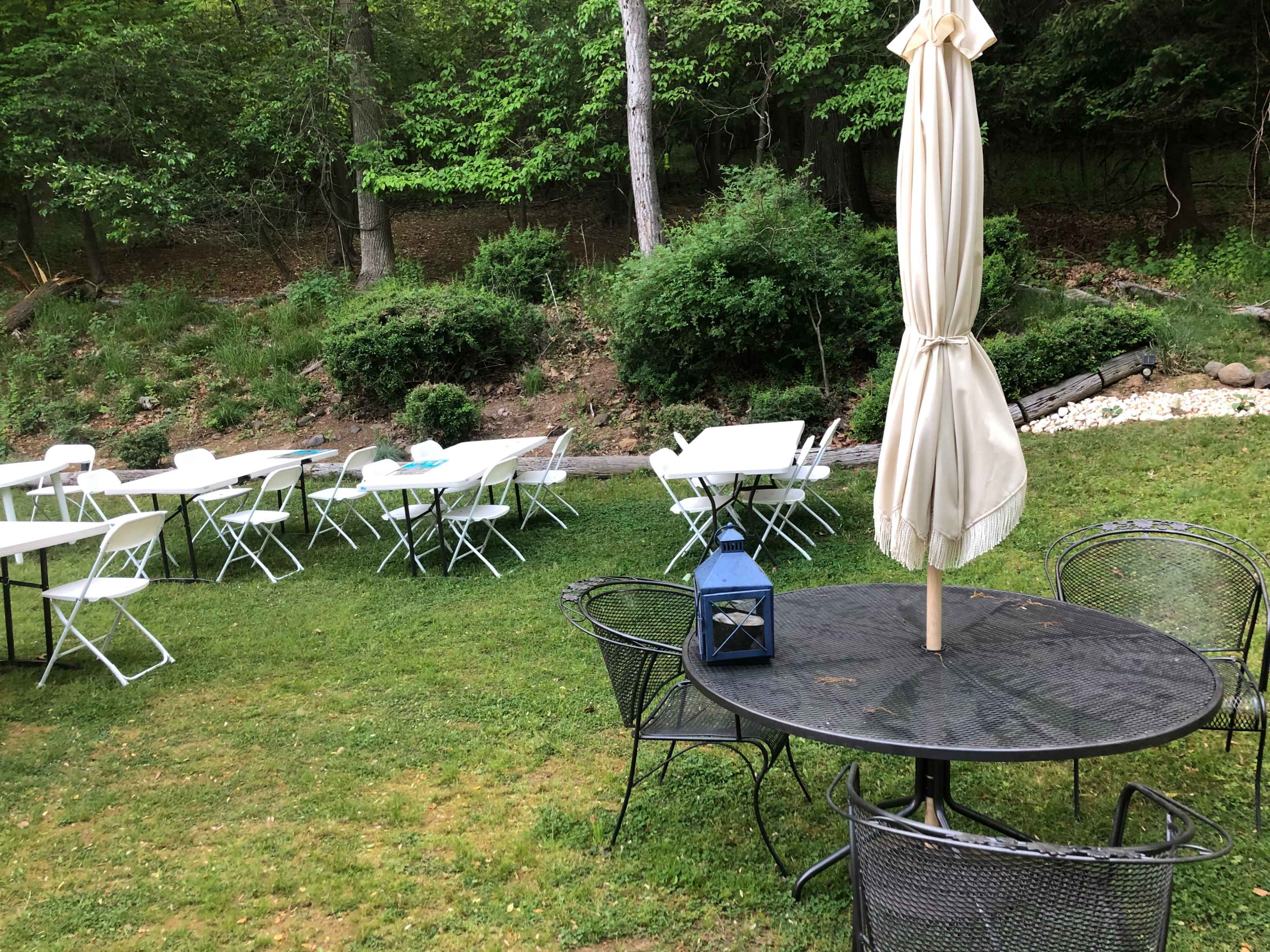 The scene shows a grassy outdoor area with several white tables and chairs arranged on the left, while a black round table and a blue lantern are positioned in the foreground.