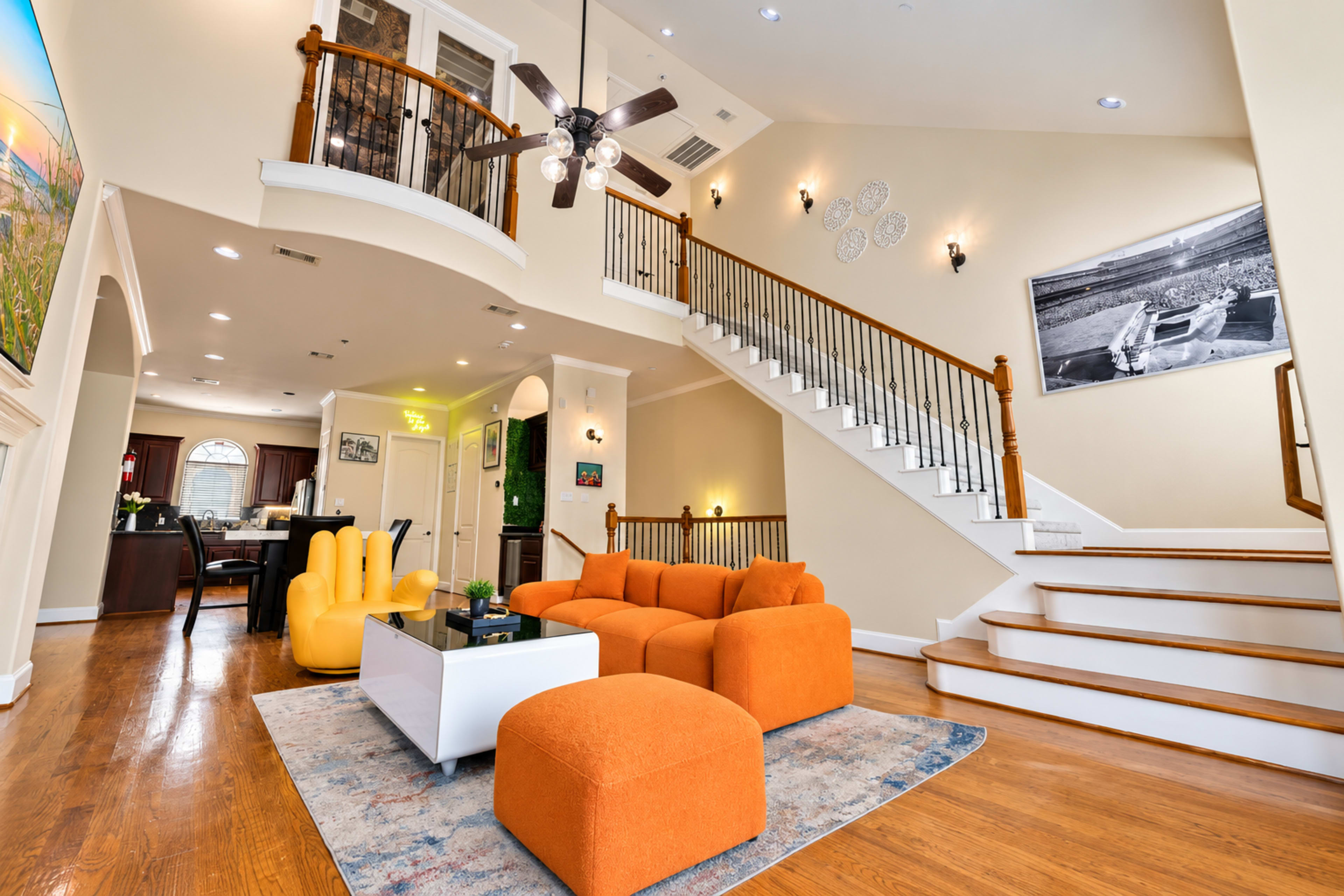 The image shows a spacious living room with an orange sectional sofa, a modern coffee table, and a staircase leading to an upper level, all adorned by decorative wall art.