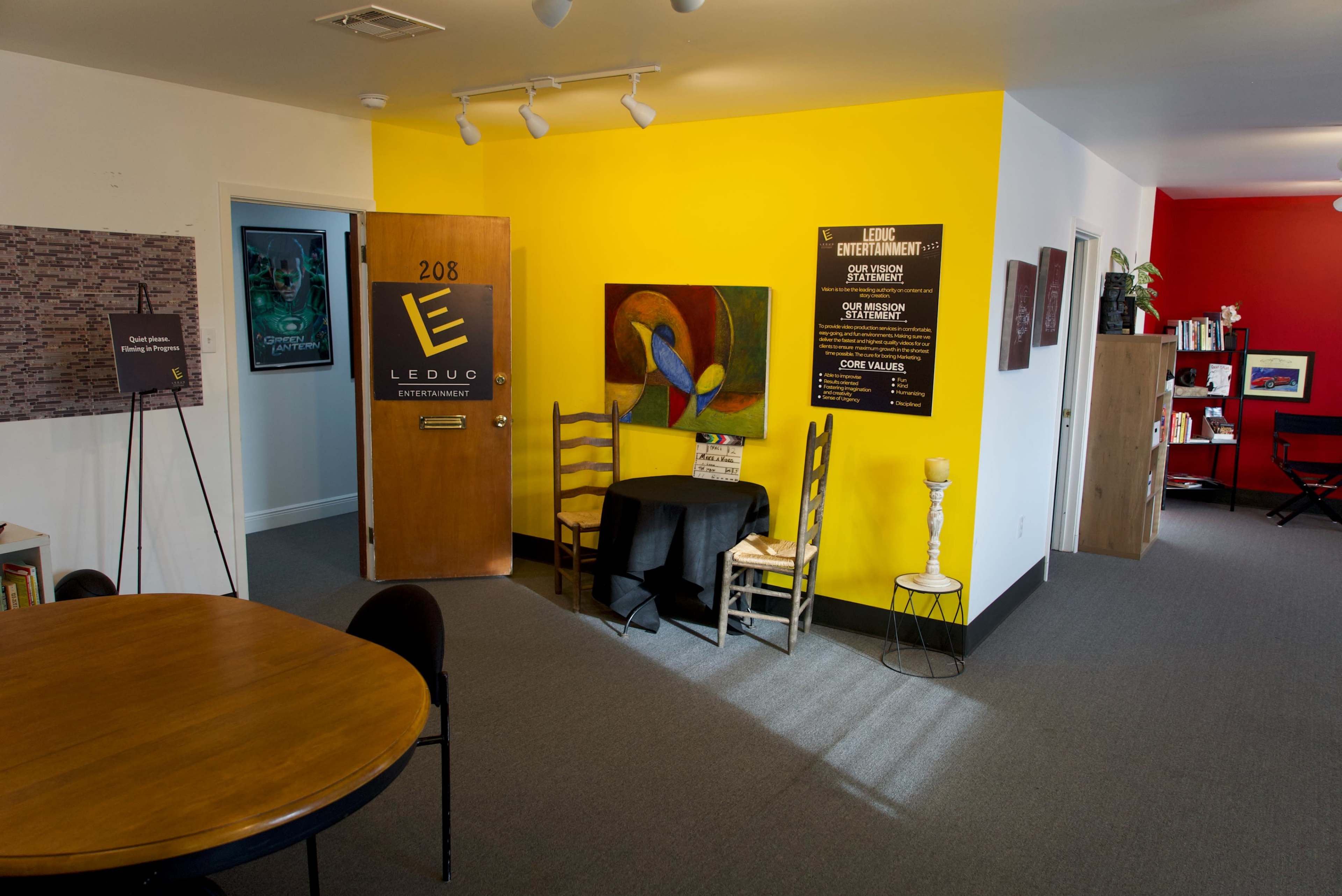 An office space featuring a yellow accent wall, a wooden door labeled "Leduc Entertainment," and a small table with chairs.