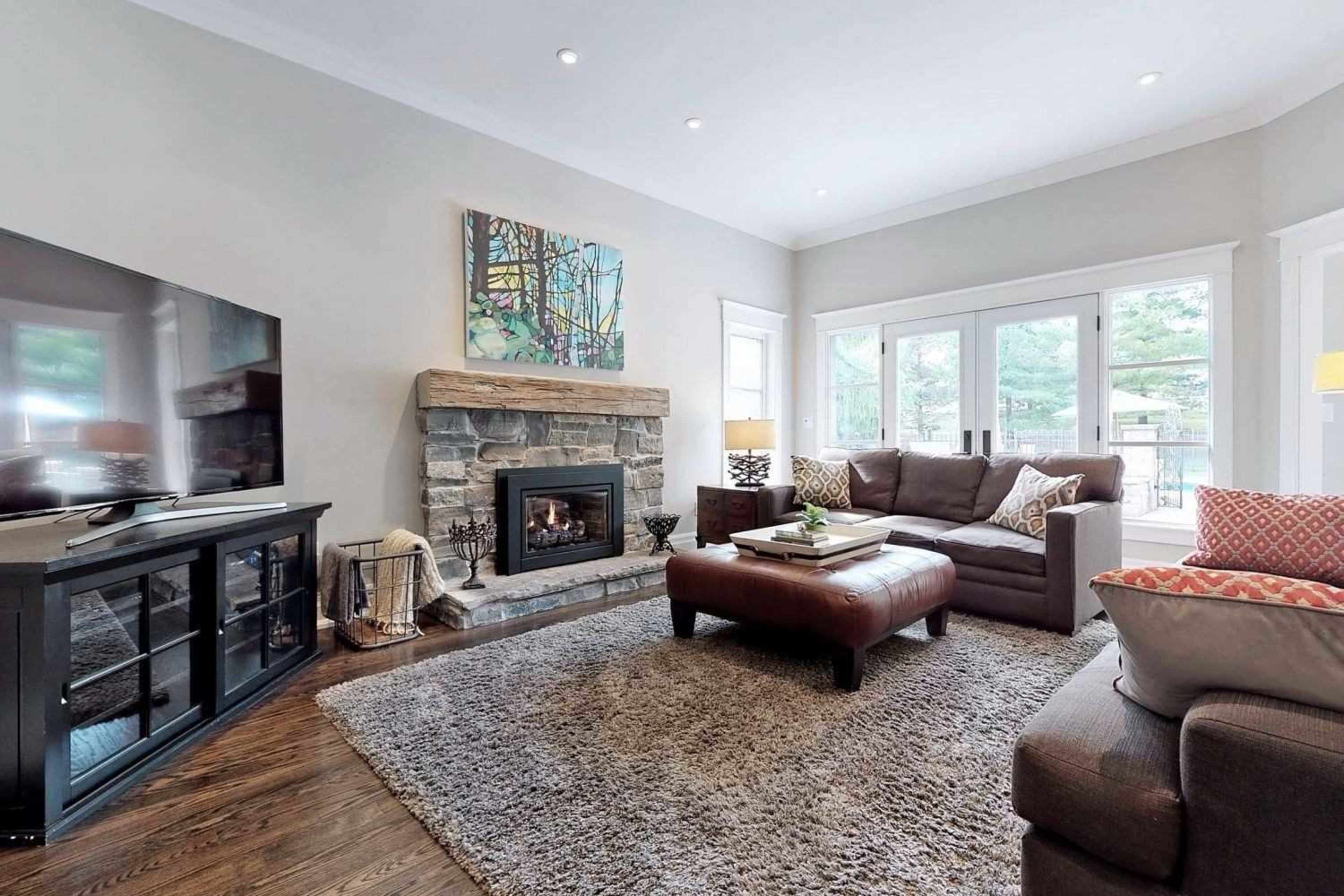 The image shows a cozy living room featuring a stone fireplace, a large television, and a comfortable seating arrangement with a coffee table on a plush rug.