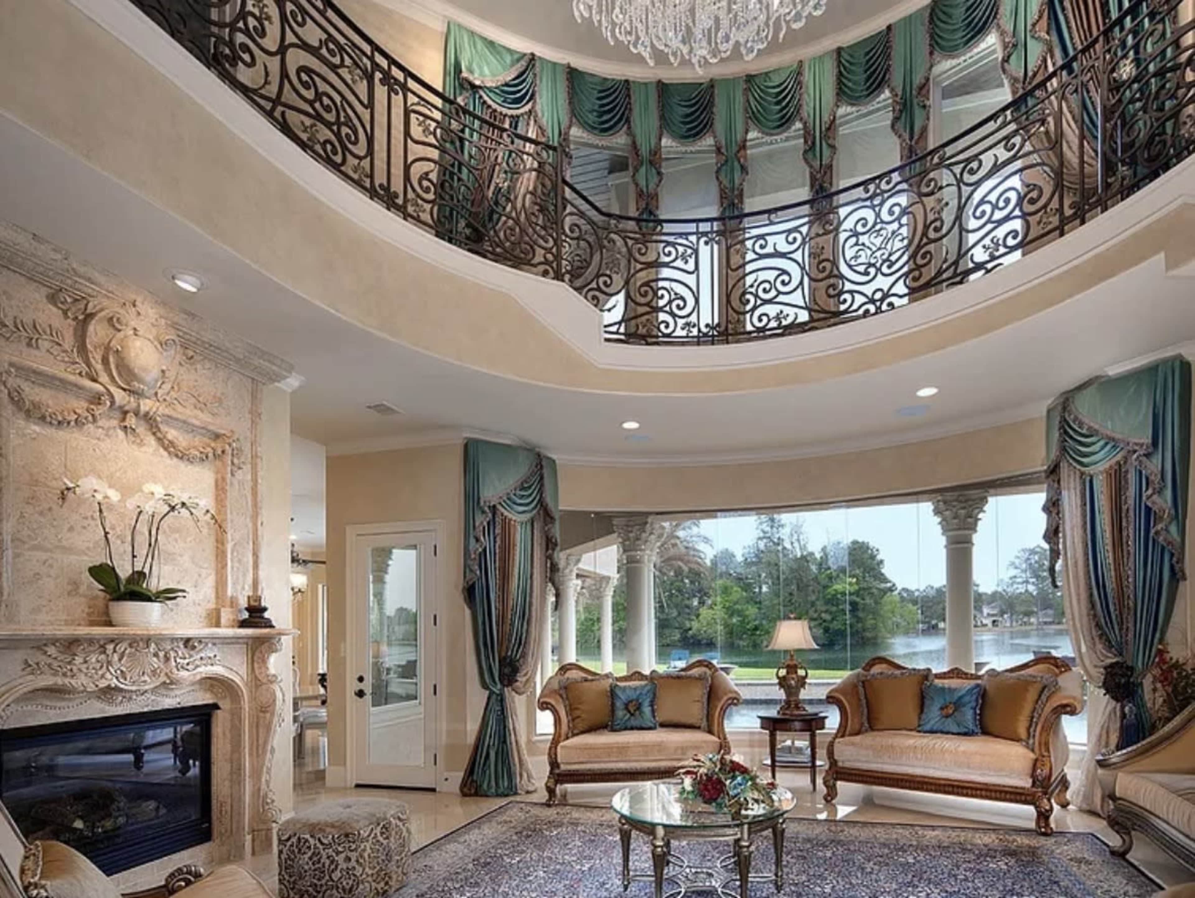 The image showcases a spacious living room with elegant furniture, featuring a grand staircase adorned with wrought-iron railings and large windows overlooking a picturesque landscape.