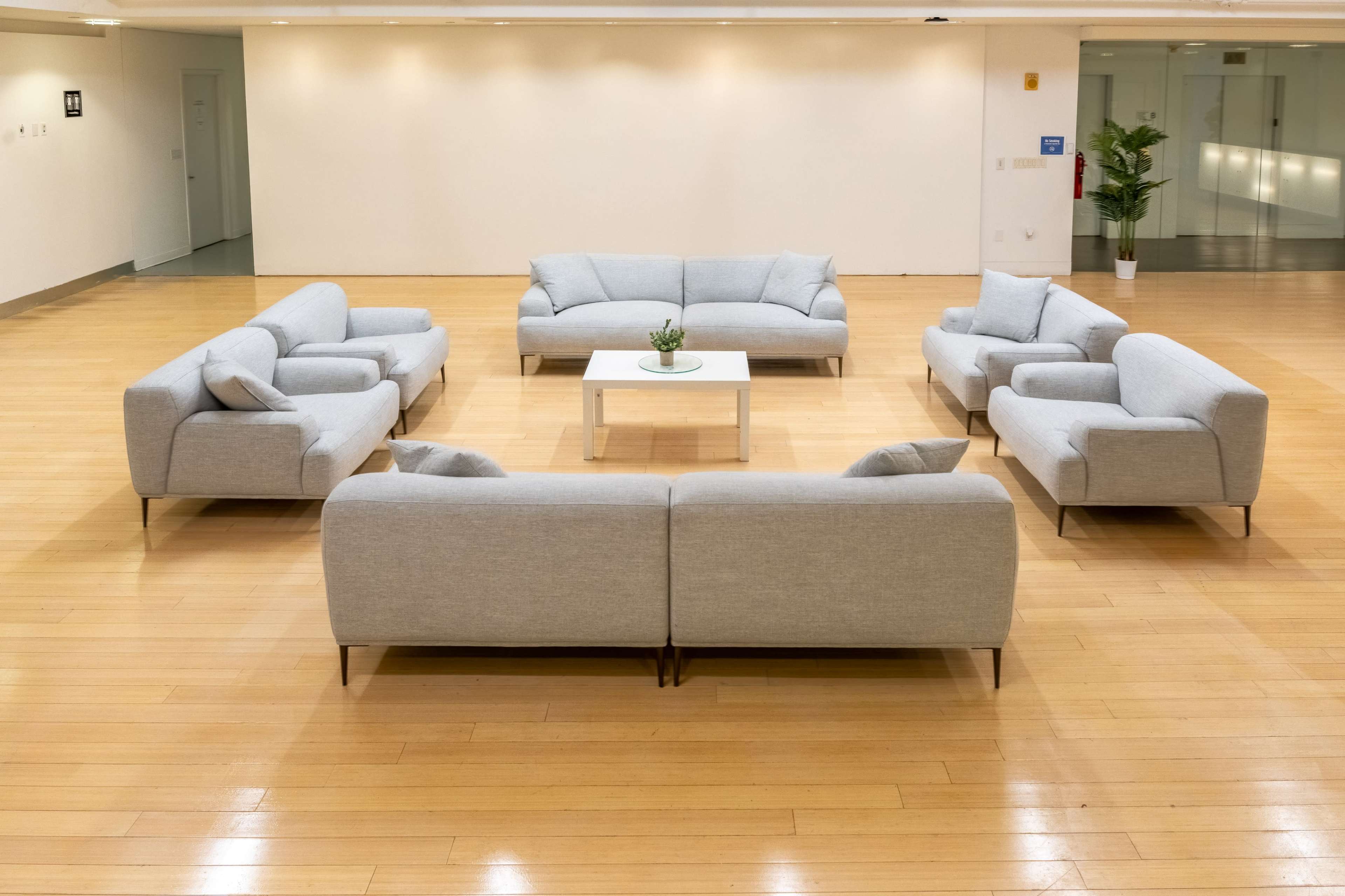 A spacious room features a circular arrangement of light gray sofas surrounding a small white coffee table.