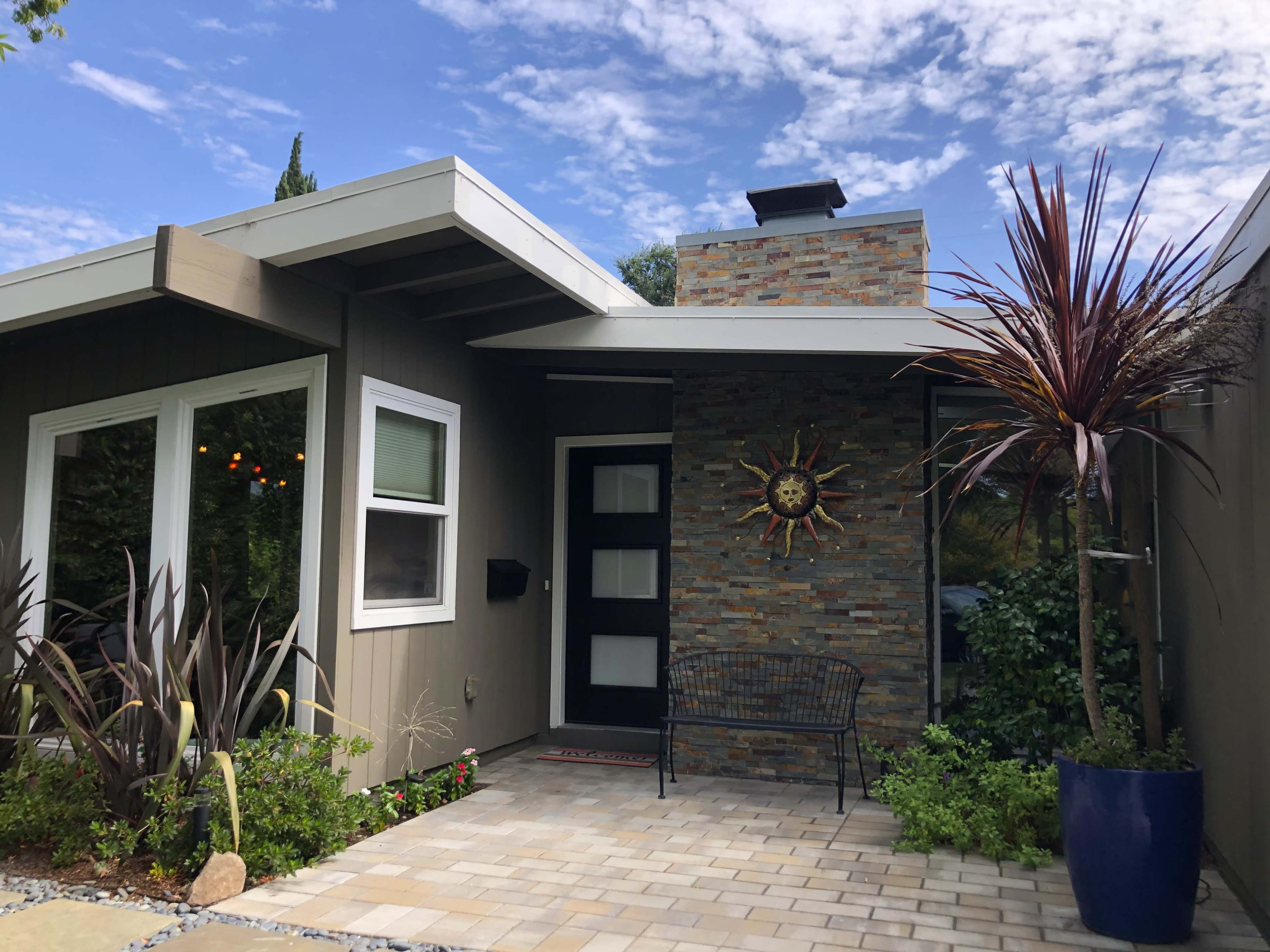 A modern house entrance with a stone accent wall, a black bench, and decorative plants in planters.