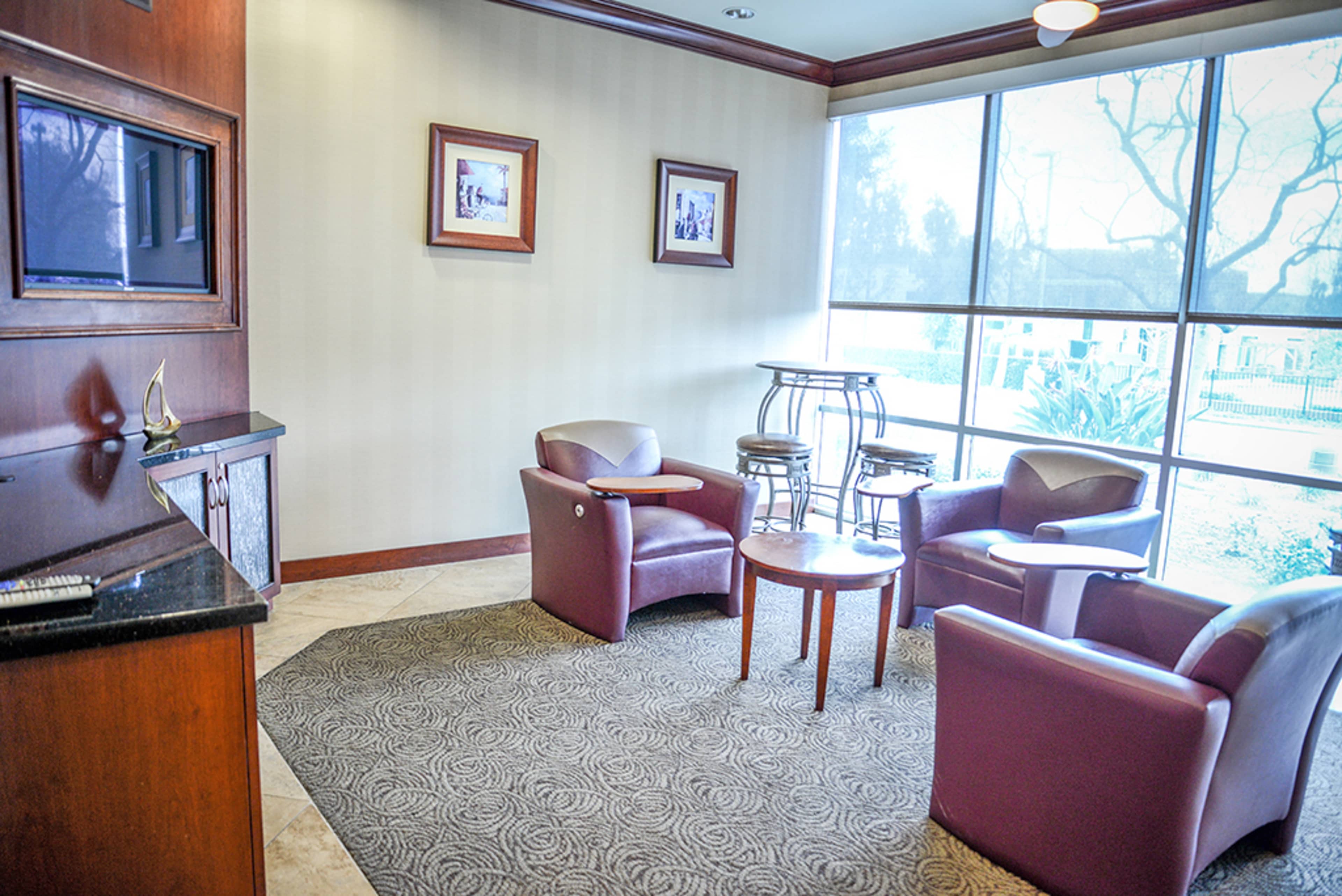 A small waiting area features two chairs, a round table, and a tall bar table near a large window.