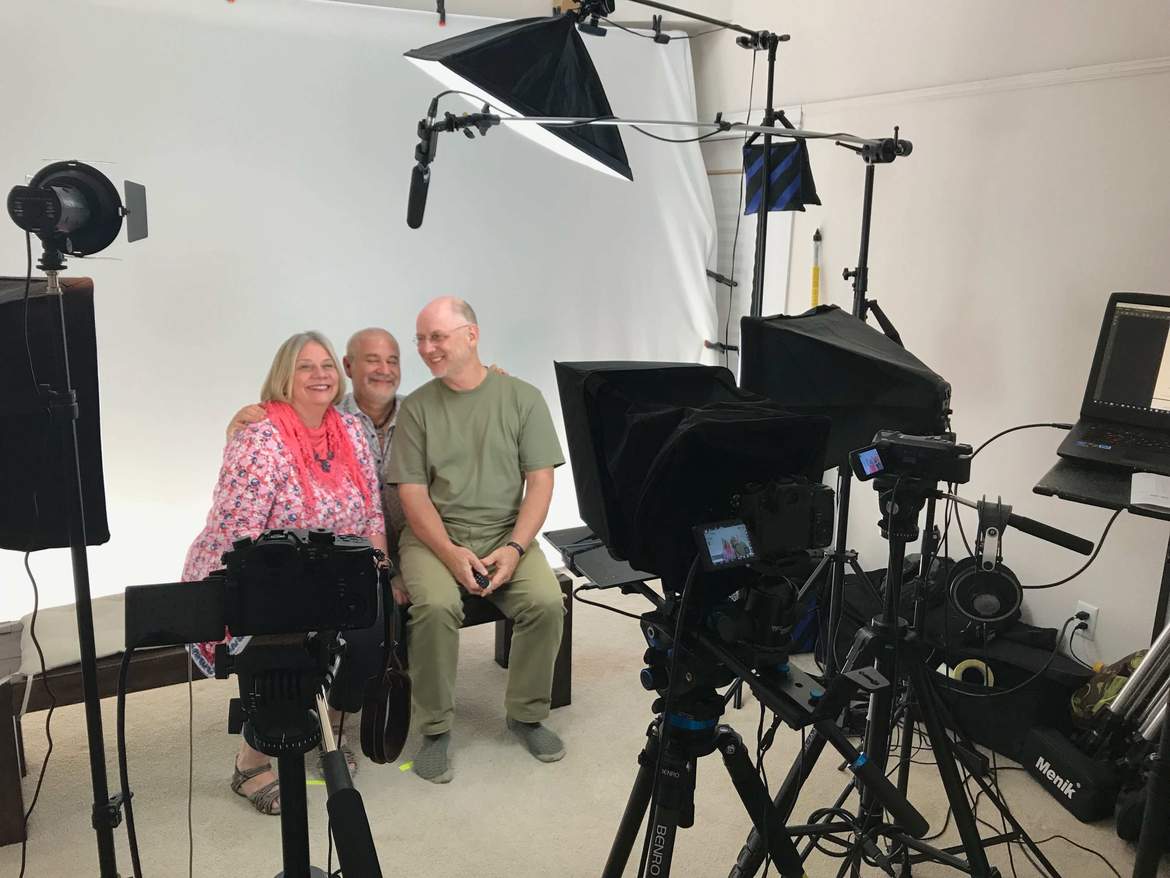 A group of three people poses for a photo in a photography studio equipped with multiple cameras and lighting equipment.