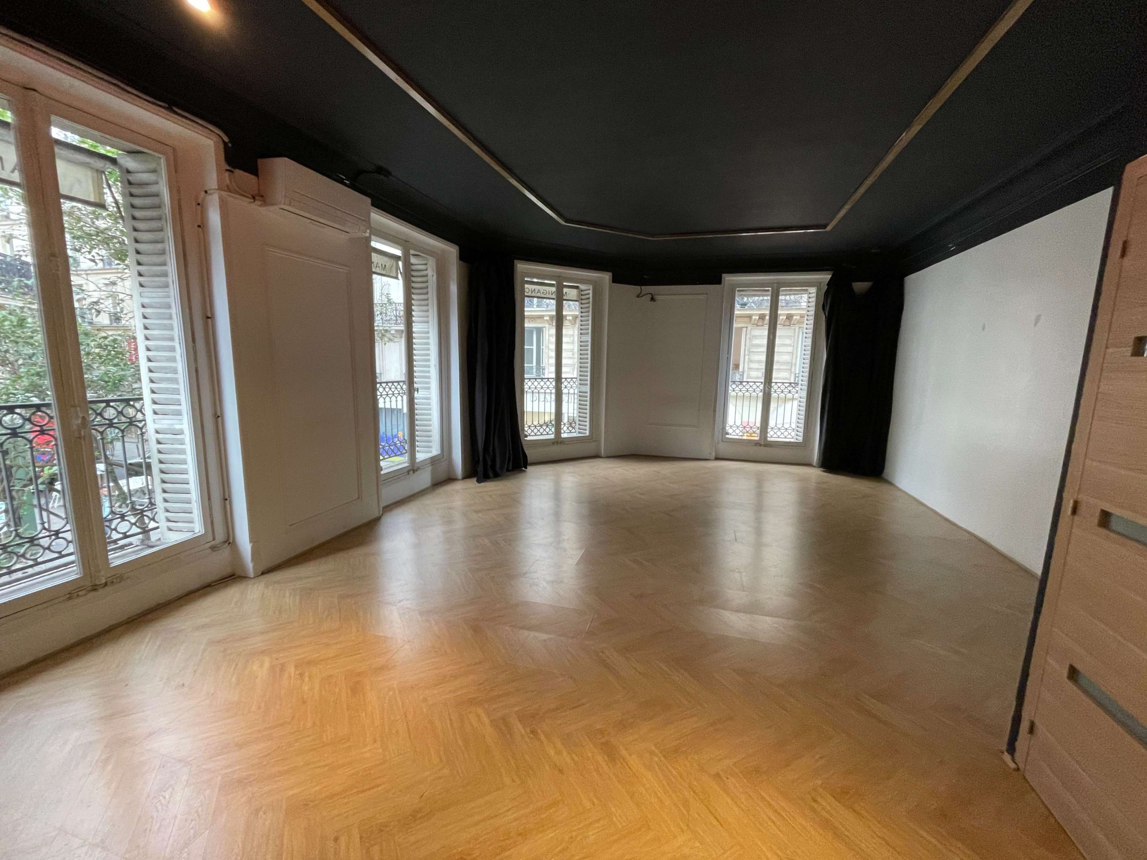 A spacious, unfurnished room with wooden flooring and large windows that open to a balcony.