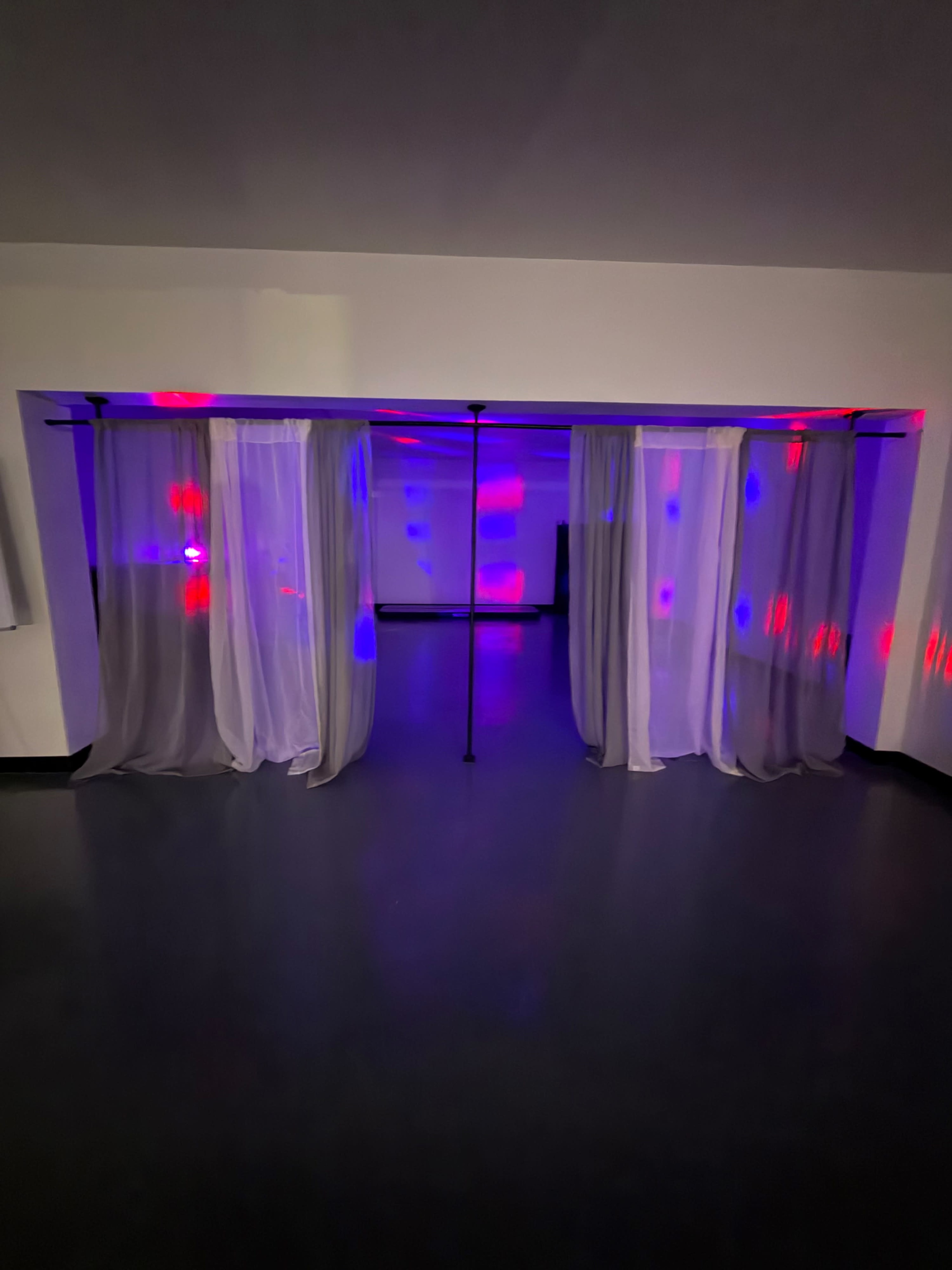 The image shows a room with sheer curtains hanging from a black structure, illuminated by multicolored lights projecting patterns on the walls.