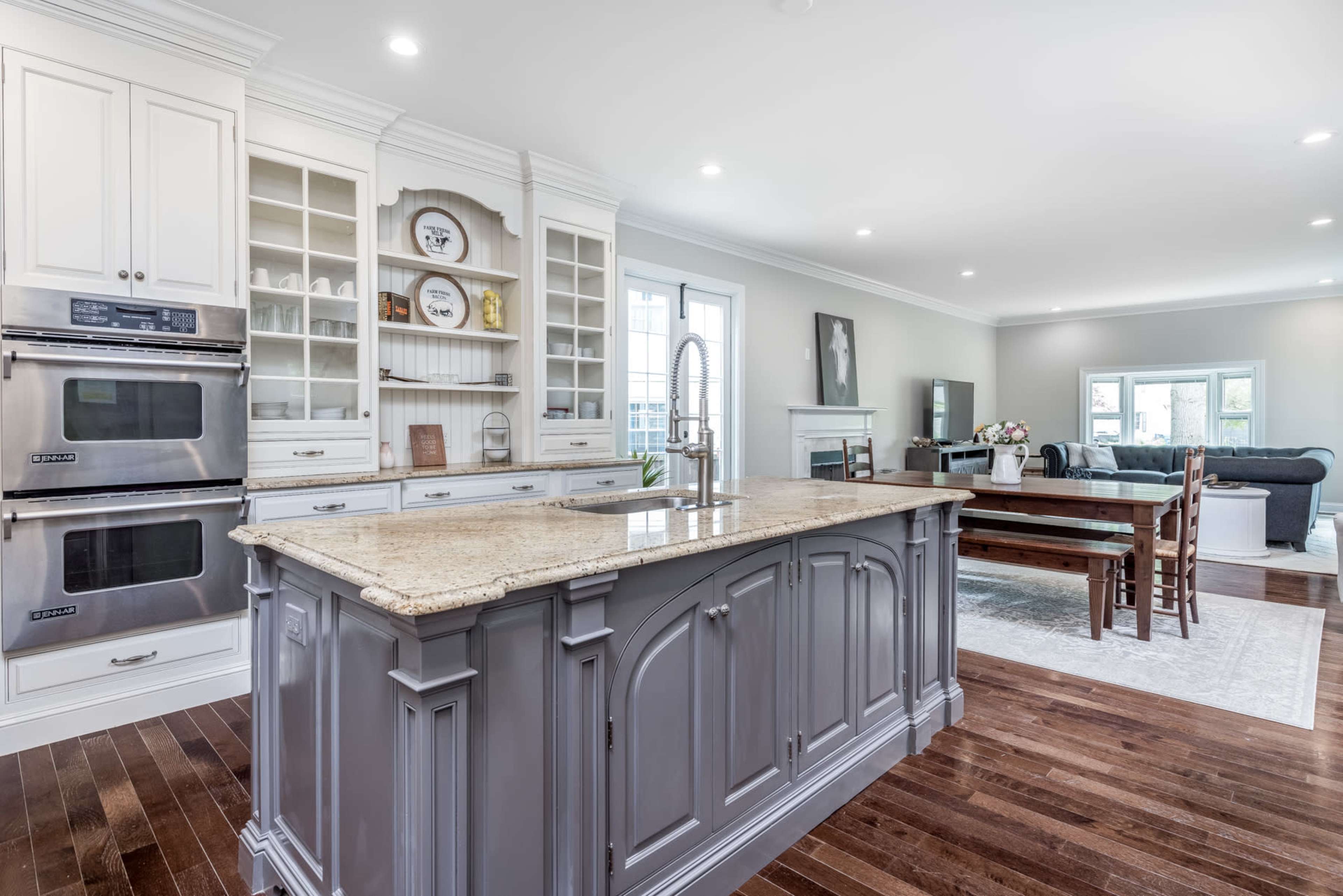 A spacious kitchen with a large island, equipped with modern appliances and wooden flooring, connected to a dining area featuring a table and chairs.