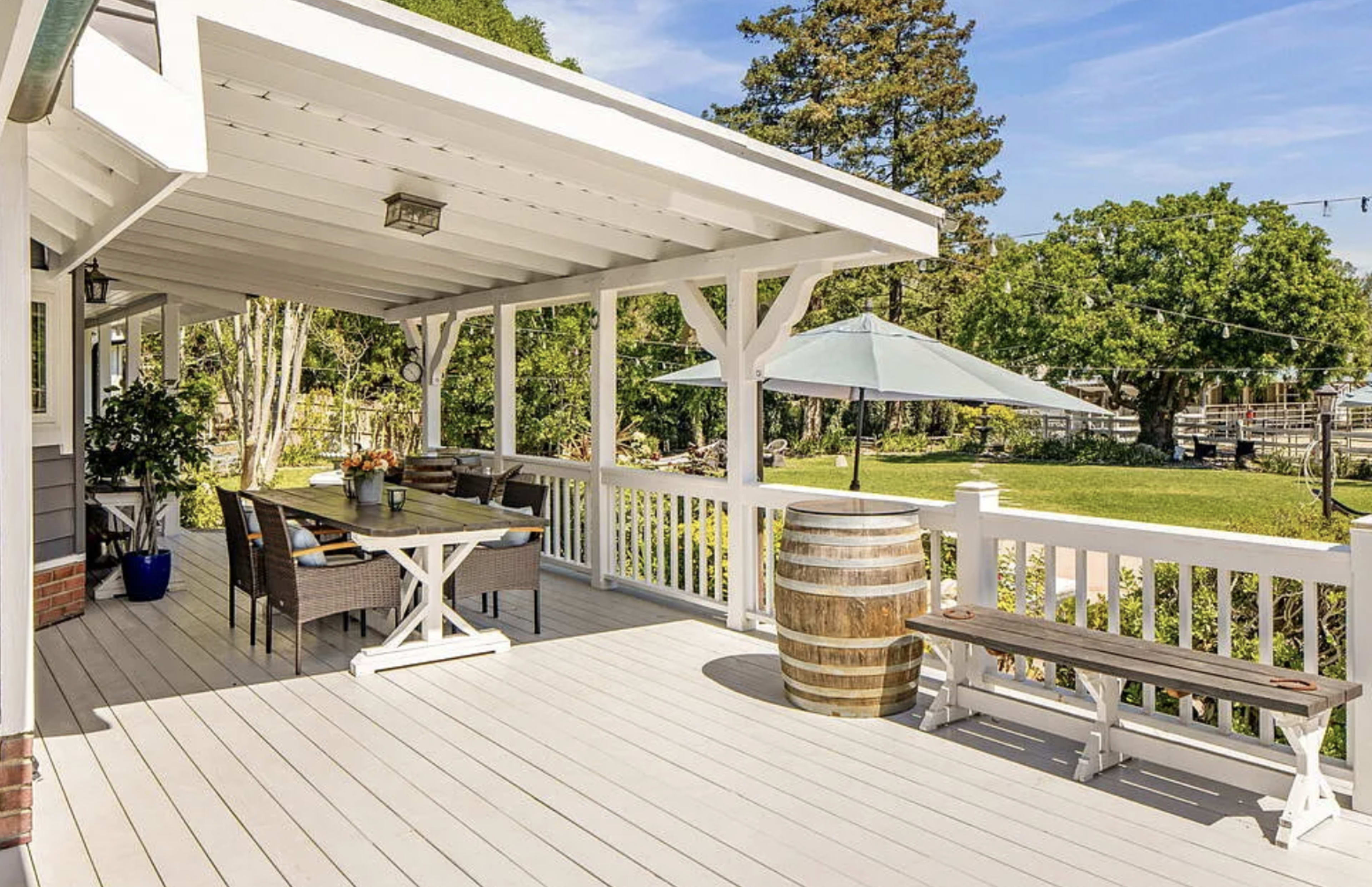 The image shows a spacious wooden deck with outdoor furniture, a large umbrella, and a barrel serving as a table.
