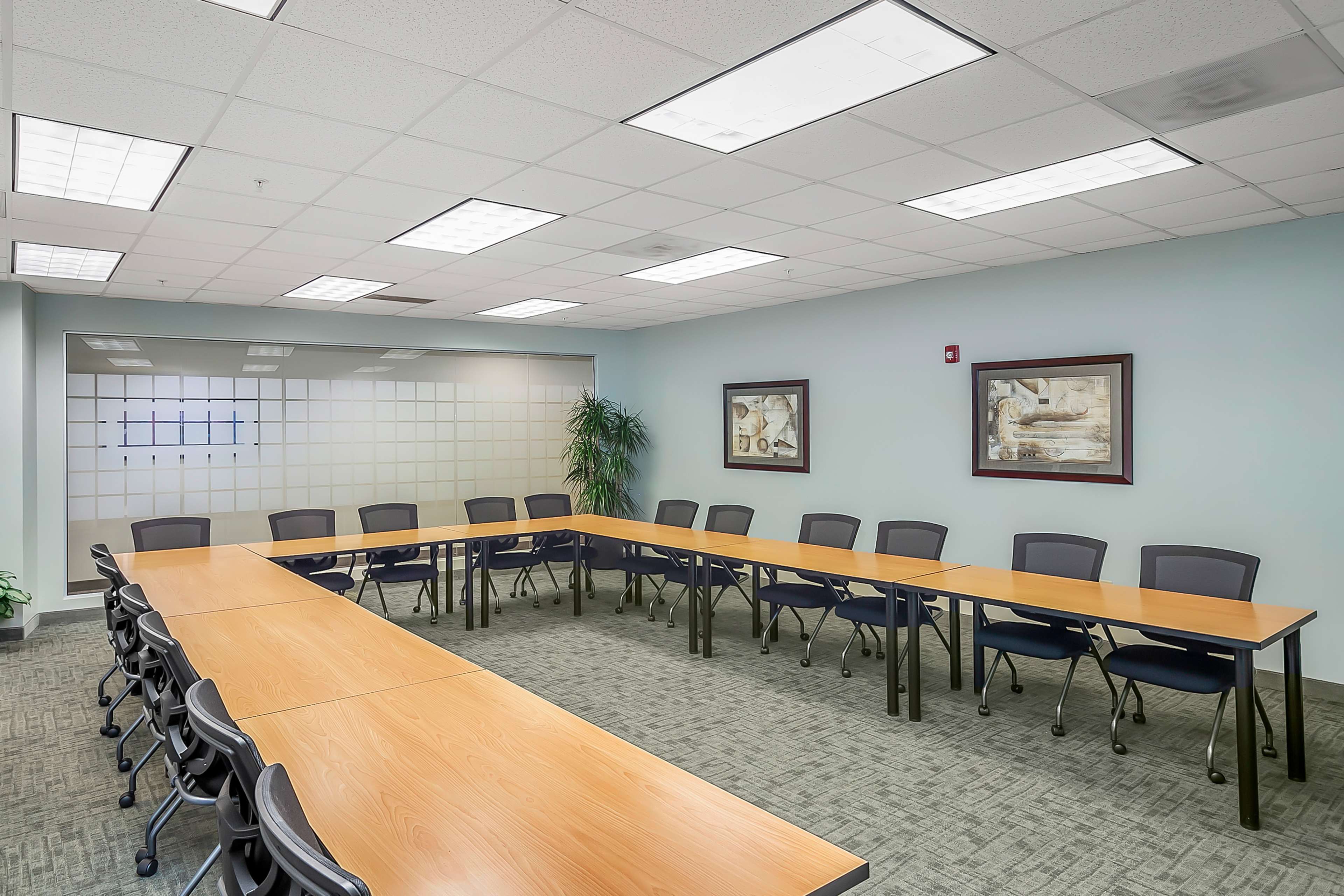 The image shows a rectangular conference room arranged with several tables and chairs, and two framed artworks on the wall.