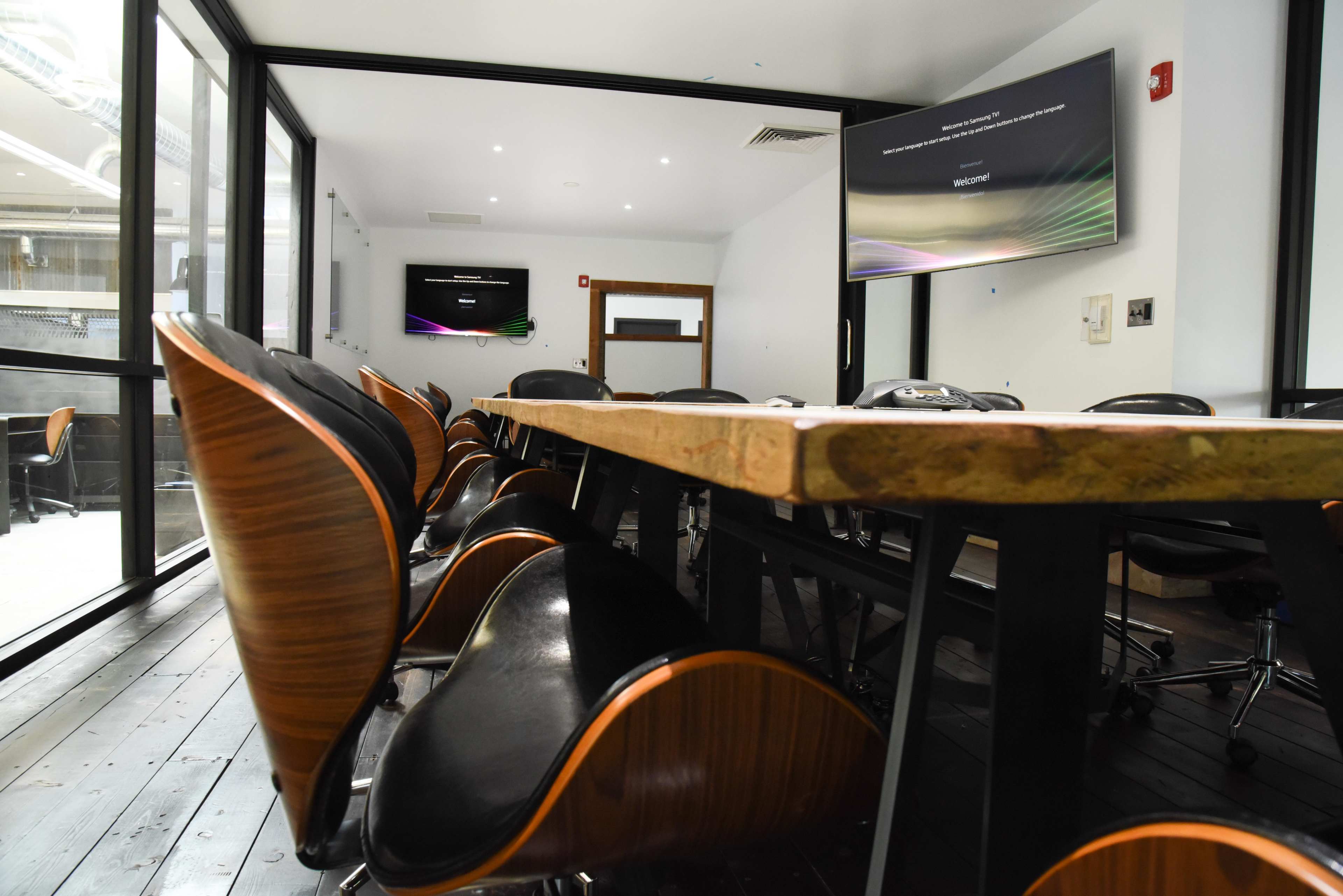 A modern conference room with a long rectangular table, black chairs, and large screens mounted on the walls.