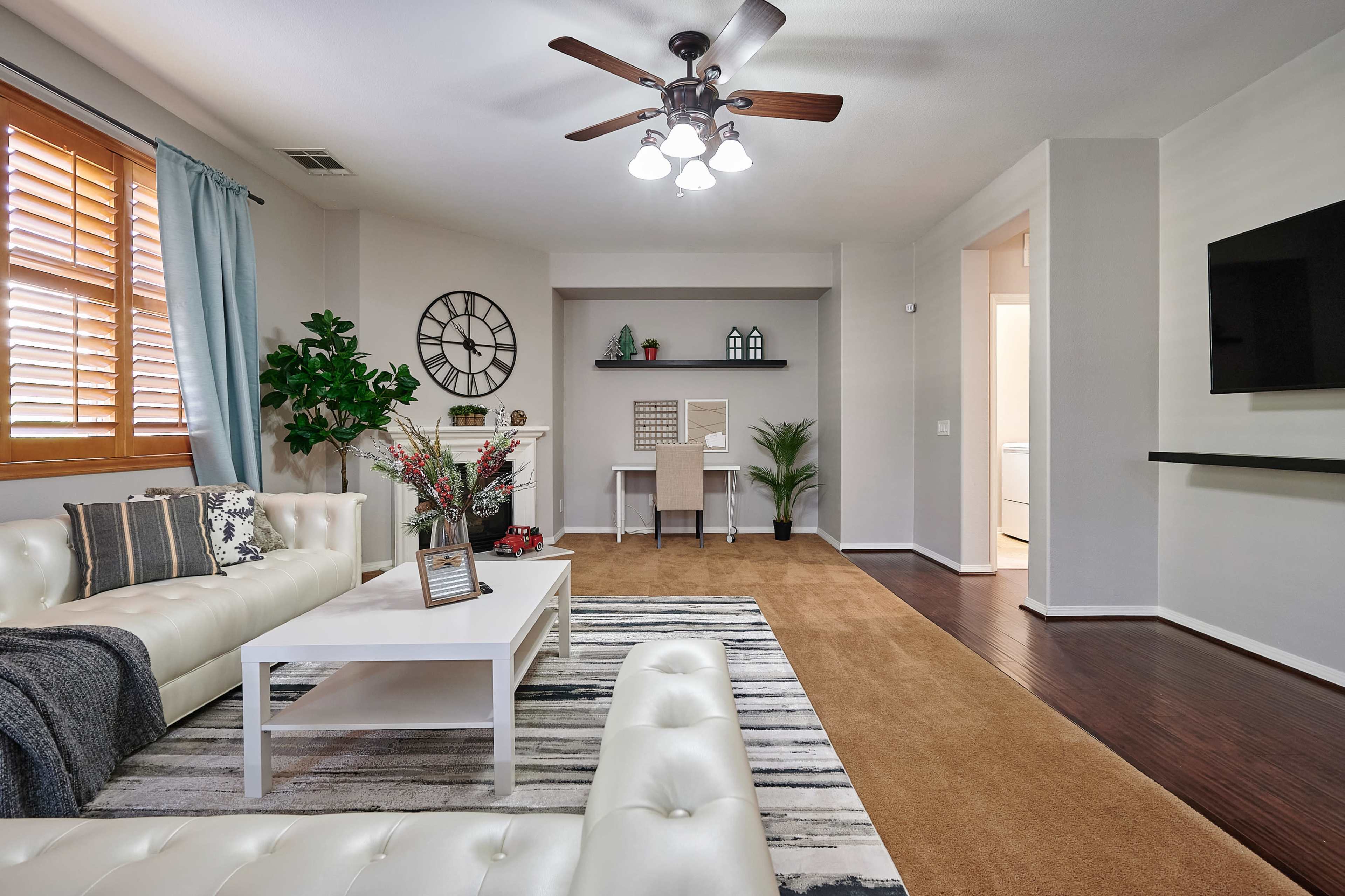 A well-decorated living room featuring a white sectional sofa, a coffee table, and a workspace with a desk against a light-colored wall.