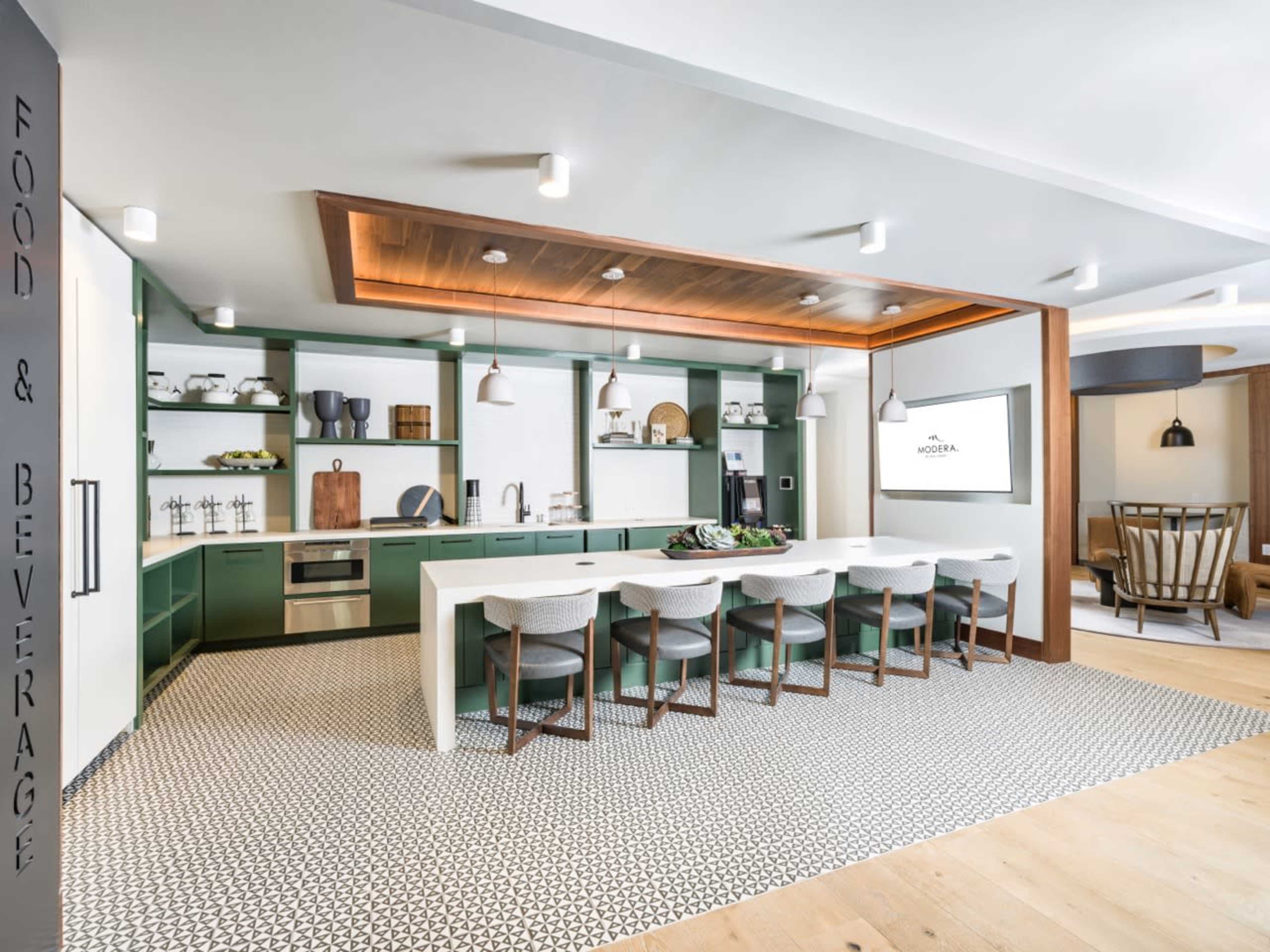 The modern kitchen features a long white island with bar stools, green cabinetry, and a patterned black and white floor.