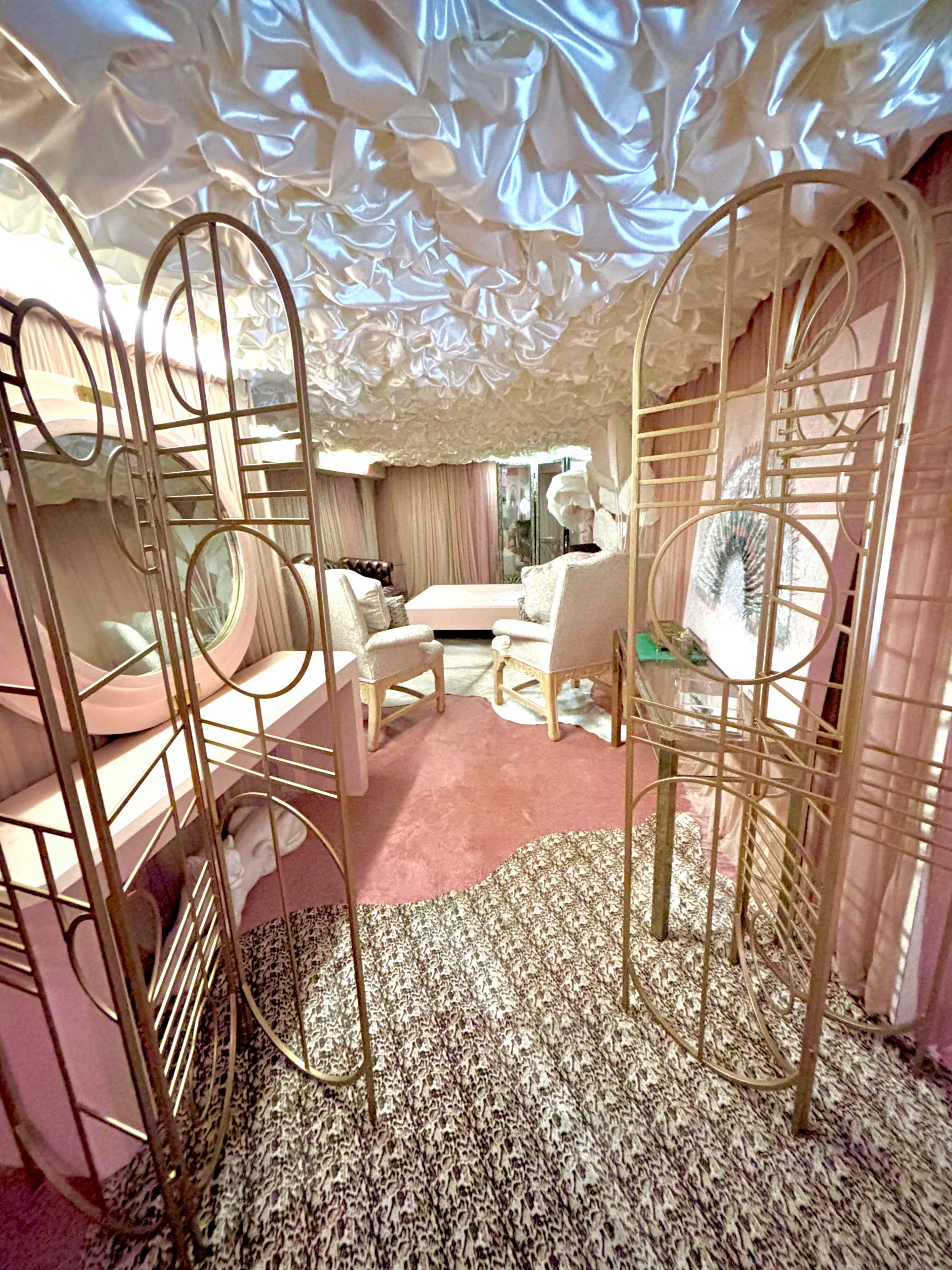 The image depicts a stylized room featuring ornate partitions, plush seating, and a textured ceiling, all in soft pastel tones.