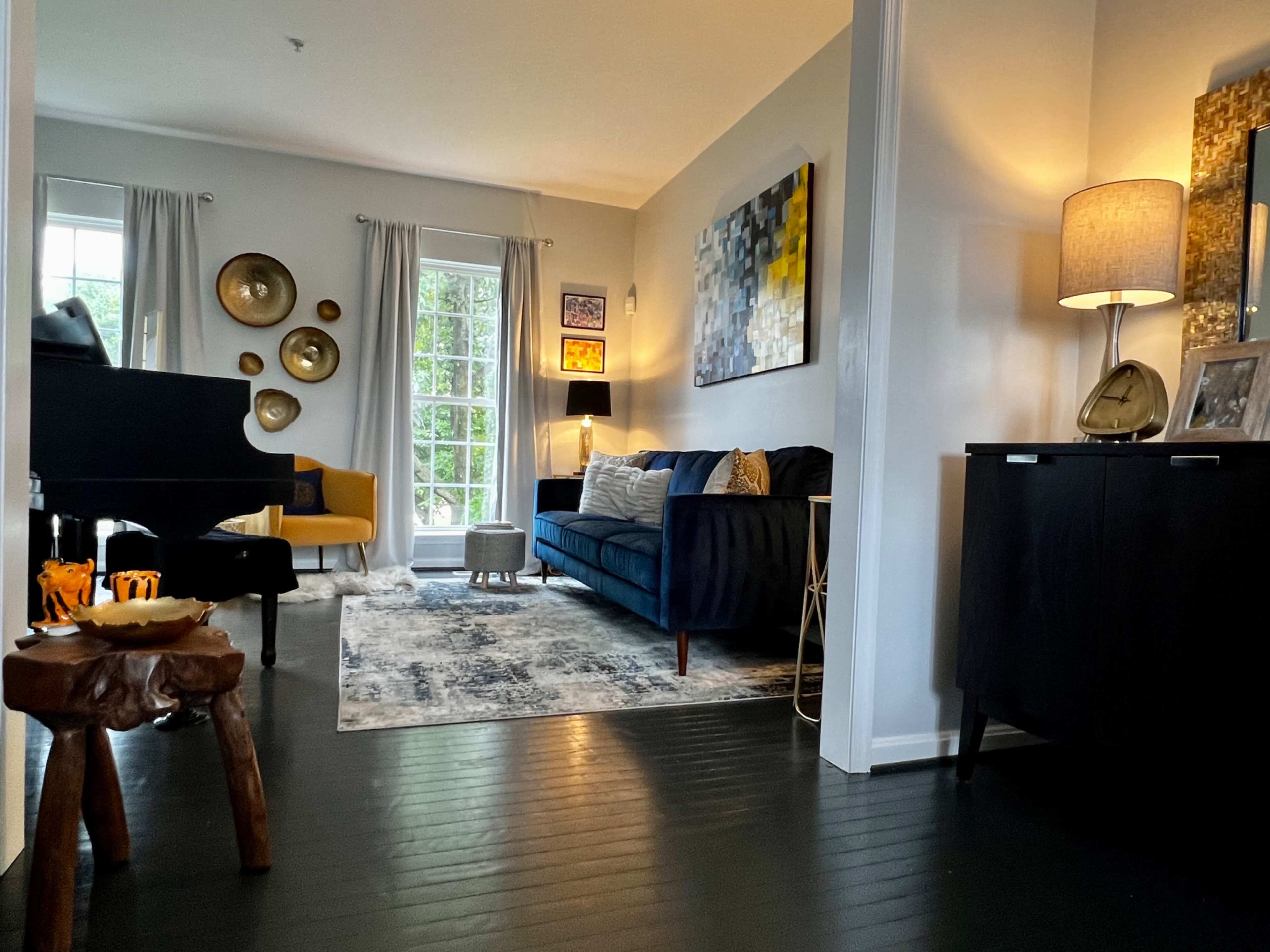 A living room with a dark blue sofa, a coffee table made from a tree stump, a grand piano, and decorative wall art, all illuminated by natural light coming through a large window.