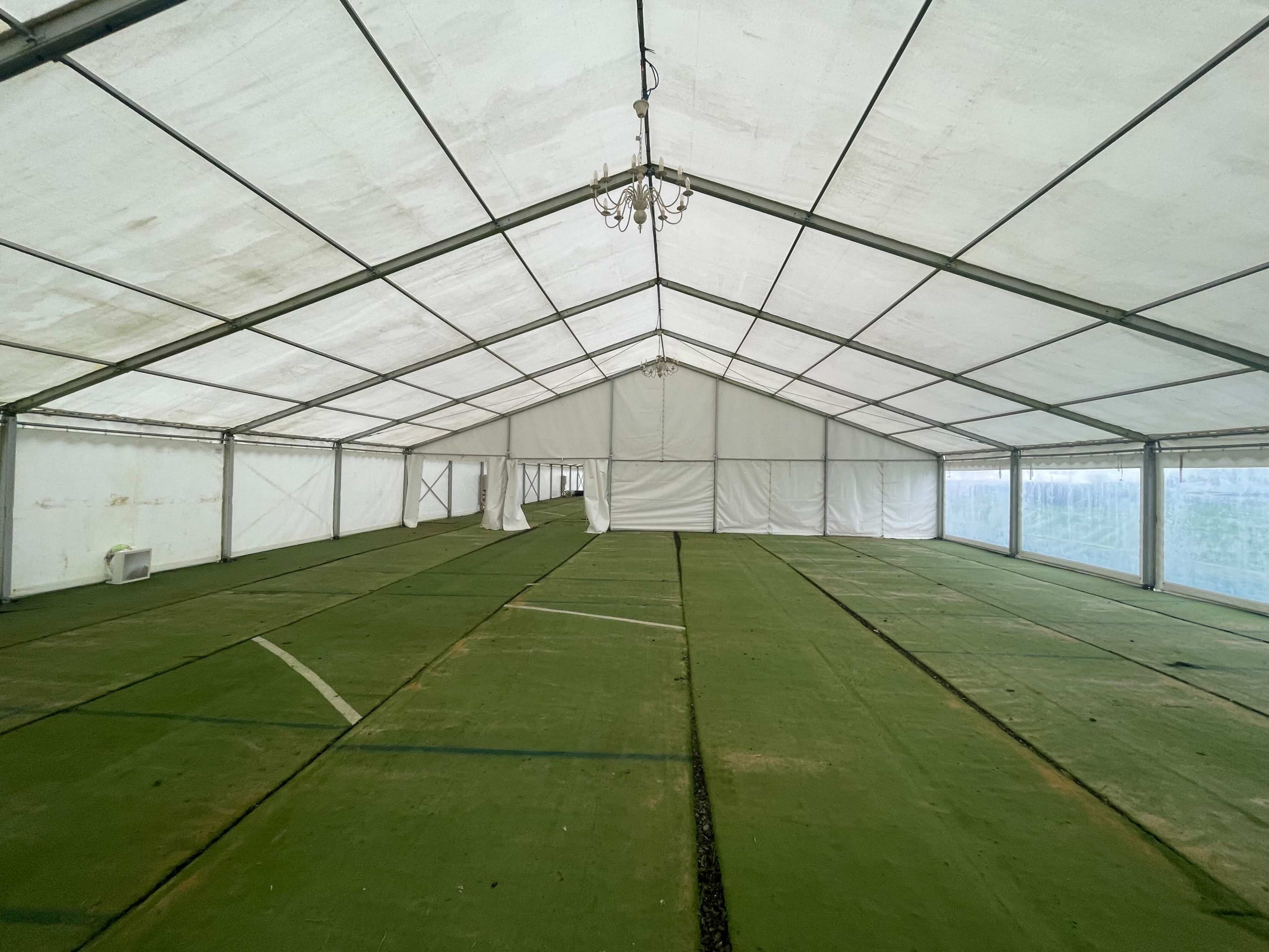 The image shows the interior of a large, empty tent with green flooring and white walls.