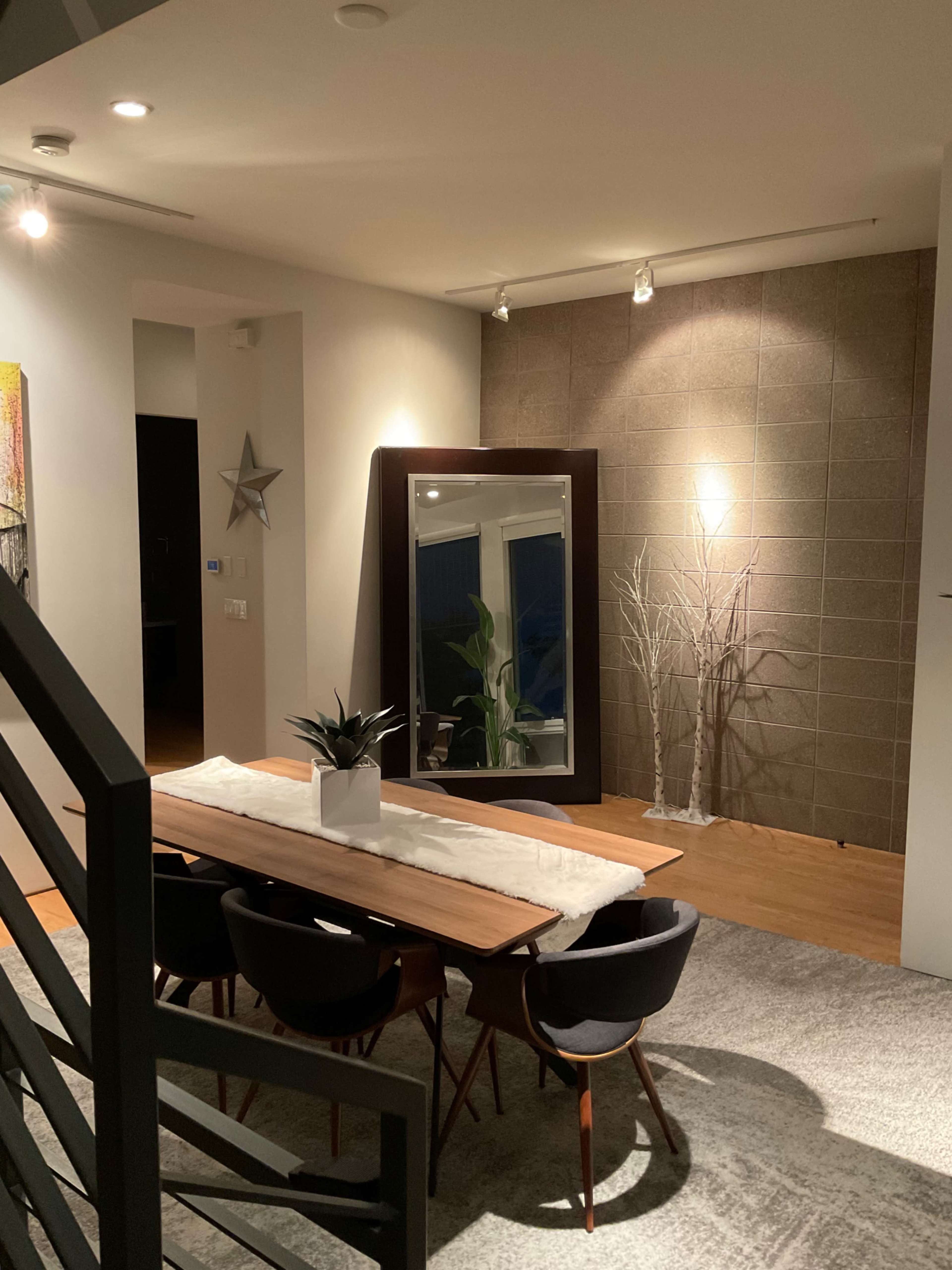 A dining area features a wooden table with black chairs, a large mirror on the wall, and a decorative plant centerpiece.