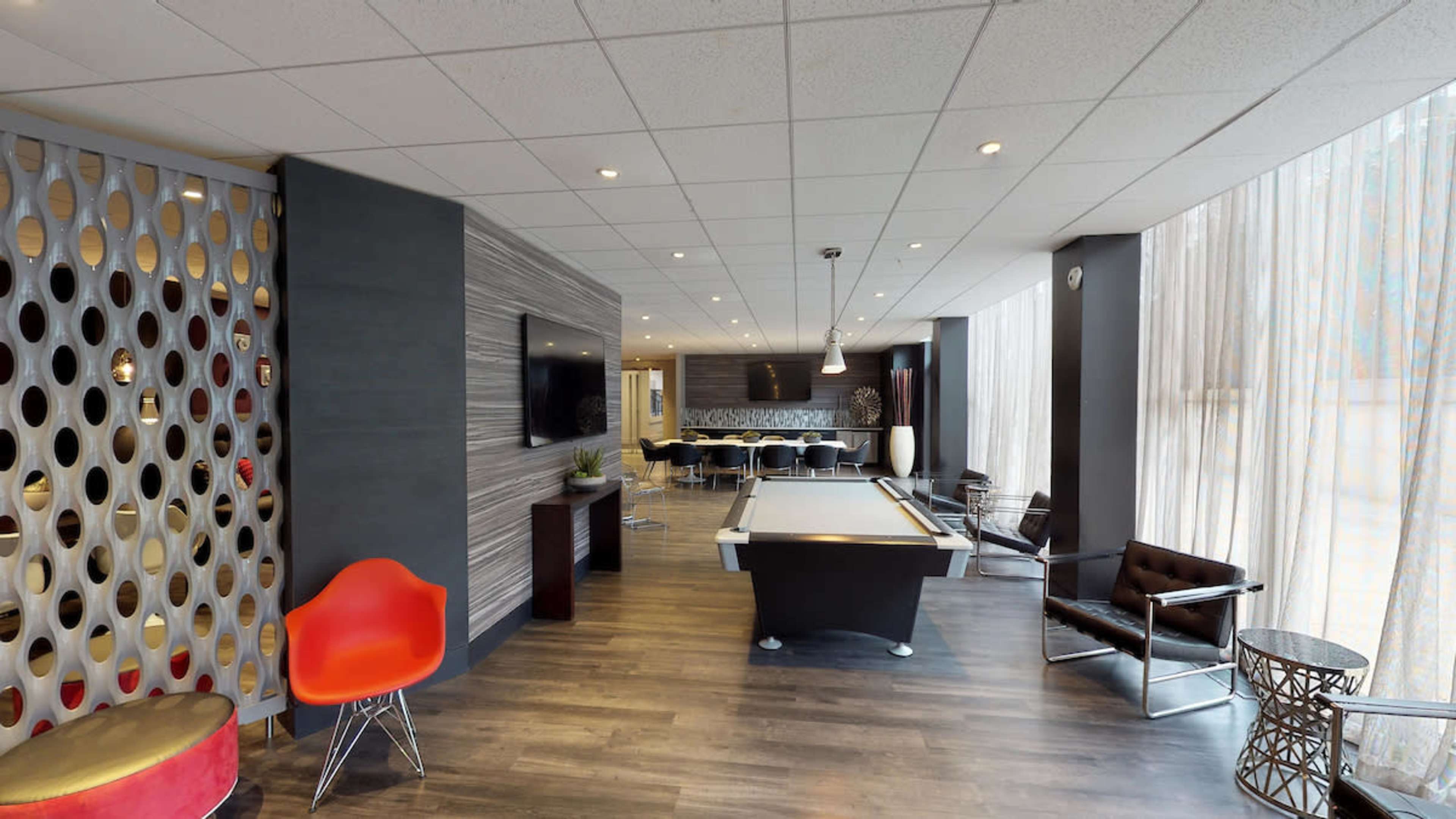 A modern lounge area featuring a pool table, seating, and large windows with sheer curtains.