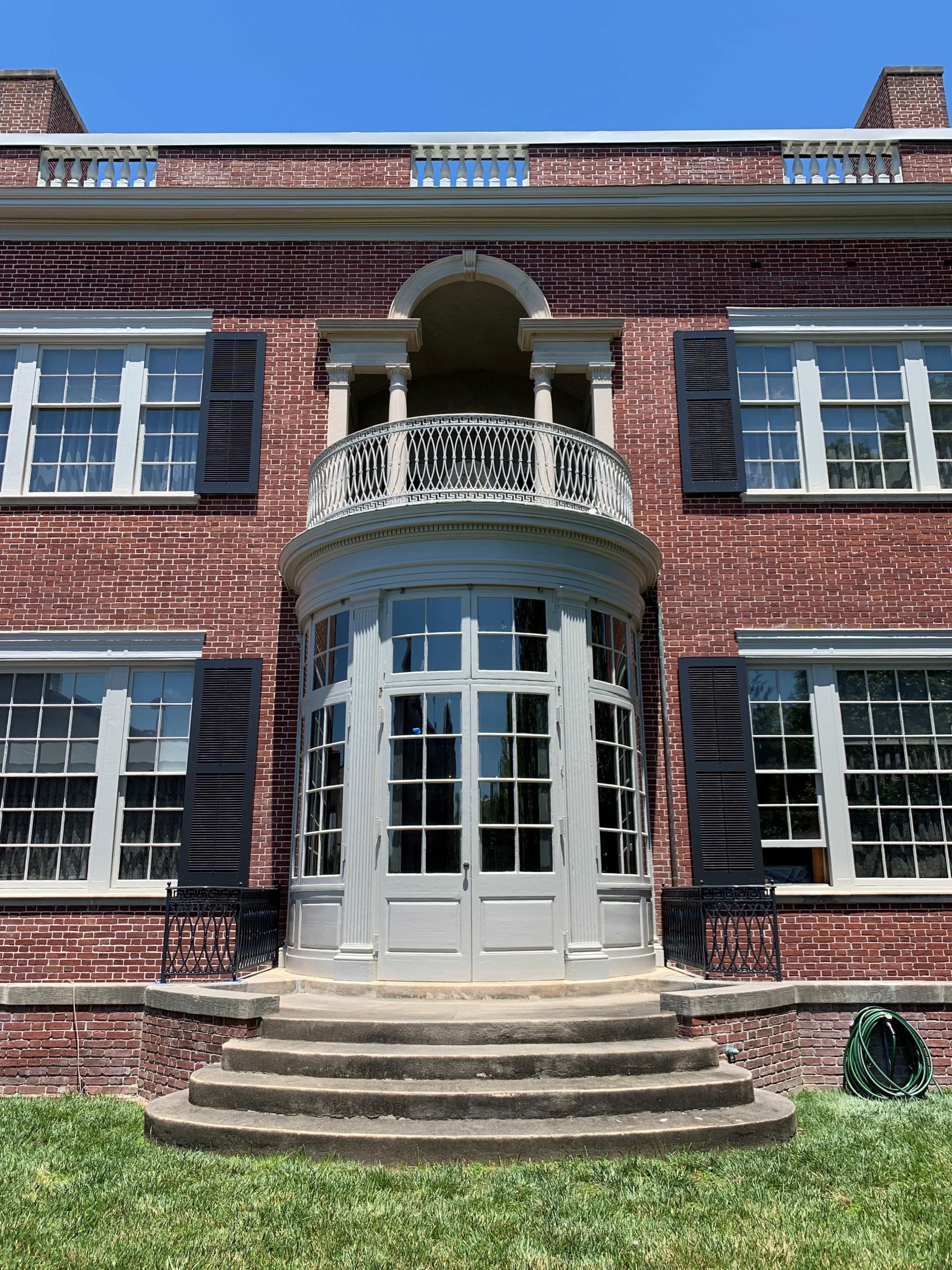 A large brick house with a rounded balcony and multiple glass doors leading to a stone staircase.