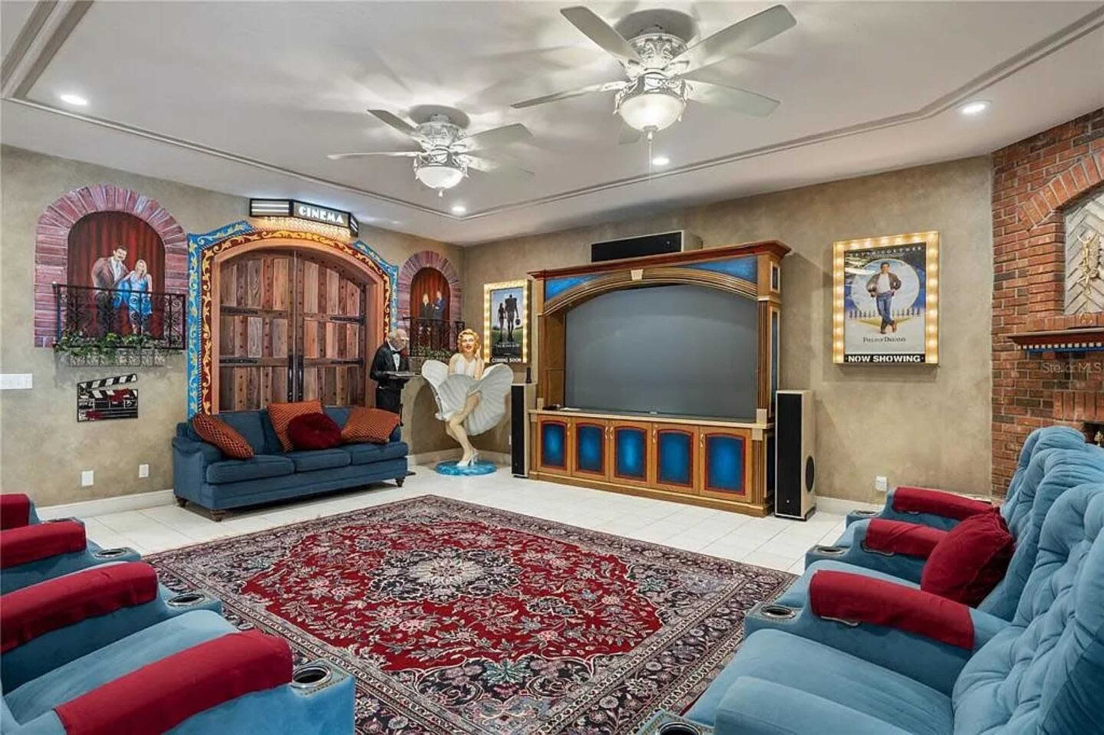The image shows a decorative home theater with blue and red seating, movie-themed artwork, and a large television on an ornate cabinet.