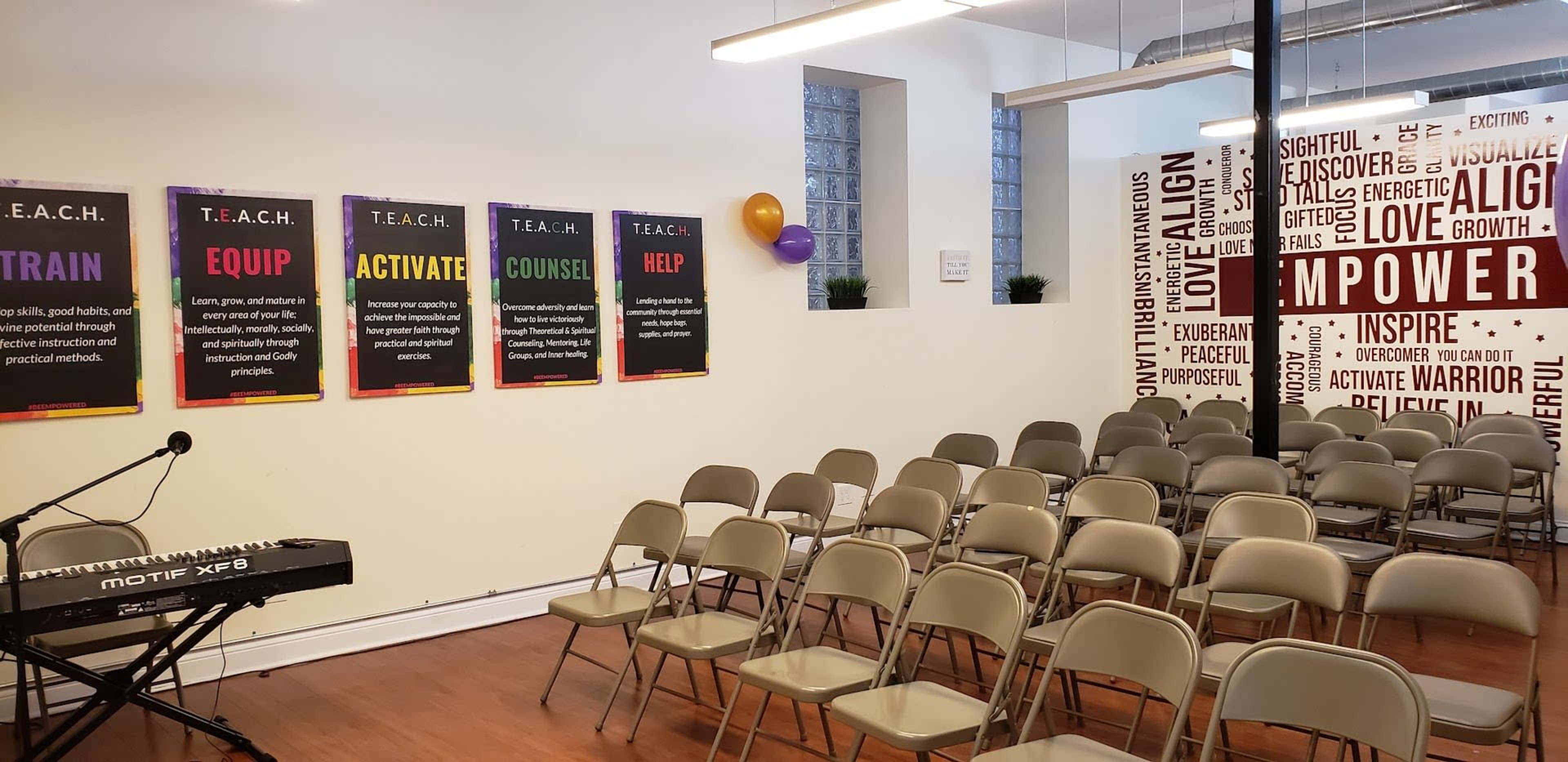 A spacious room with chairs arranged in rows facing a wall decorated with motivational posters and a keyboard on a stand.