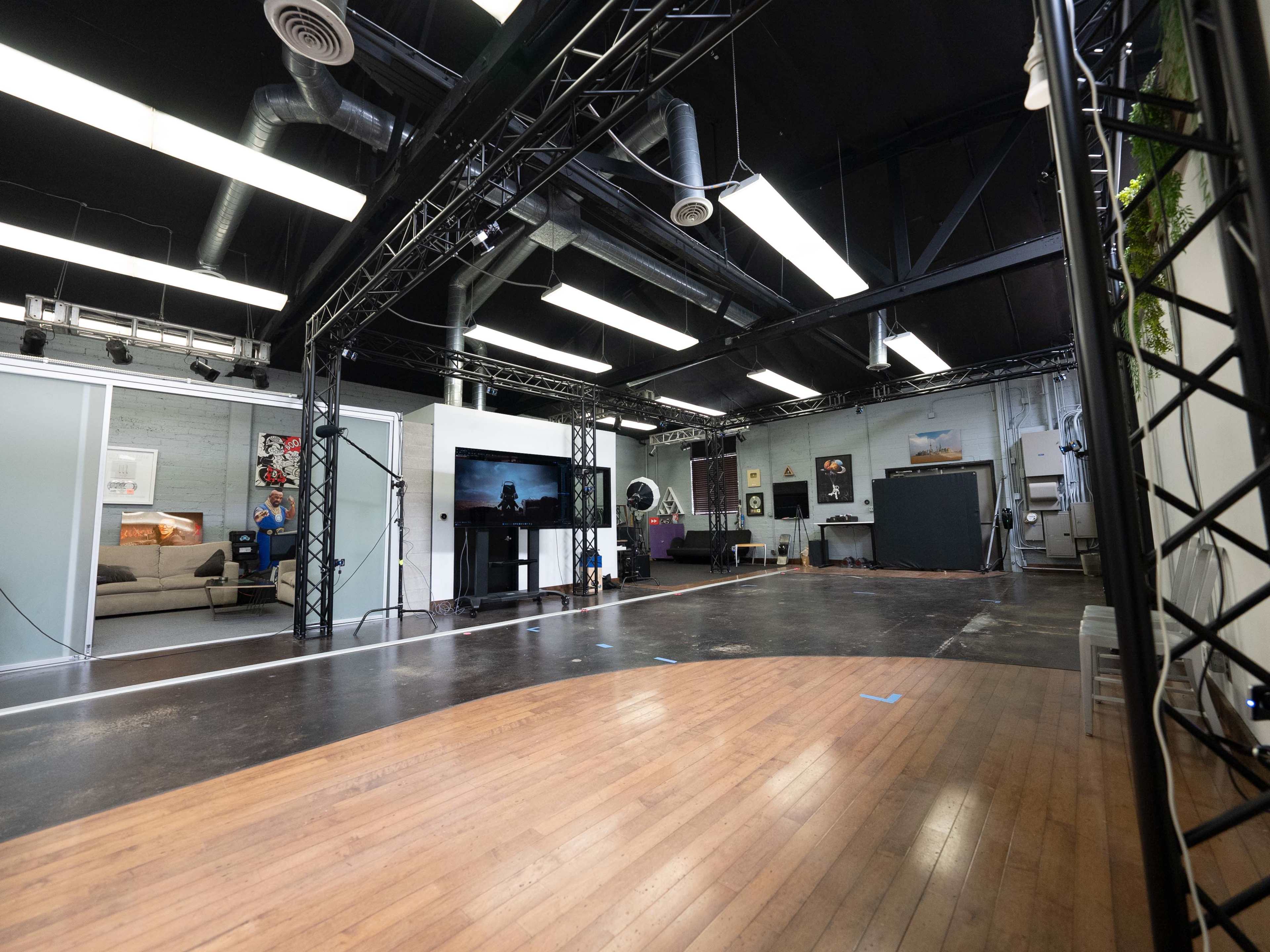 A spacious studio with a wooden floor, black steel trusses, and various decorative elements, including a television and artwork on the walls.