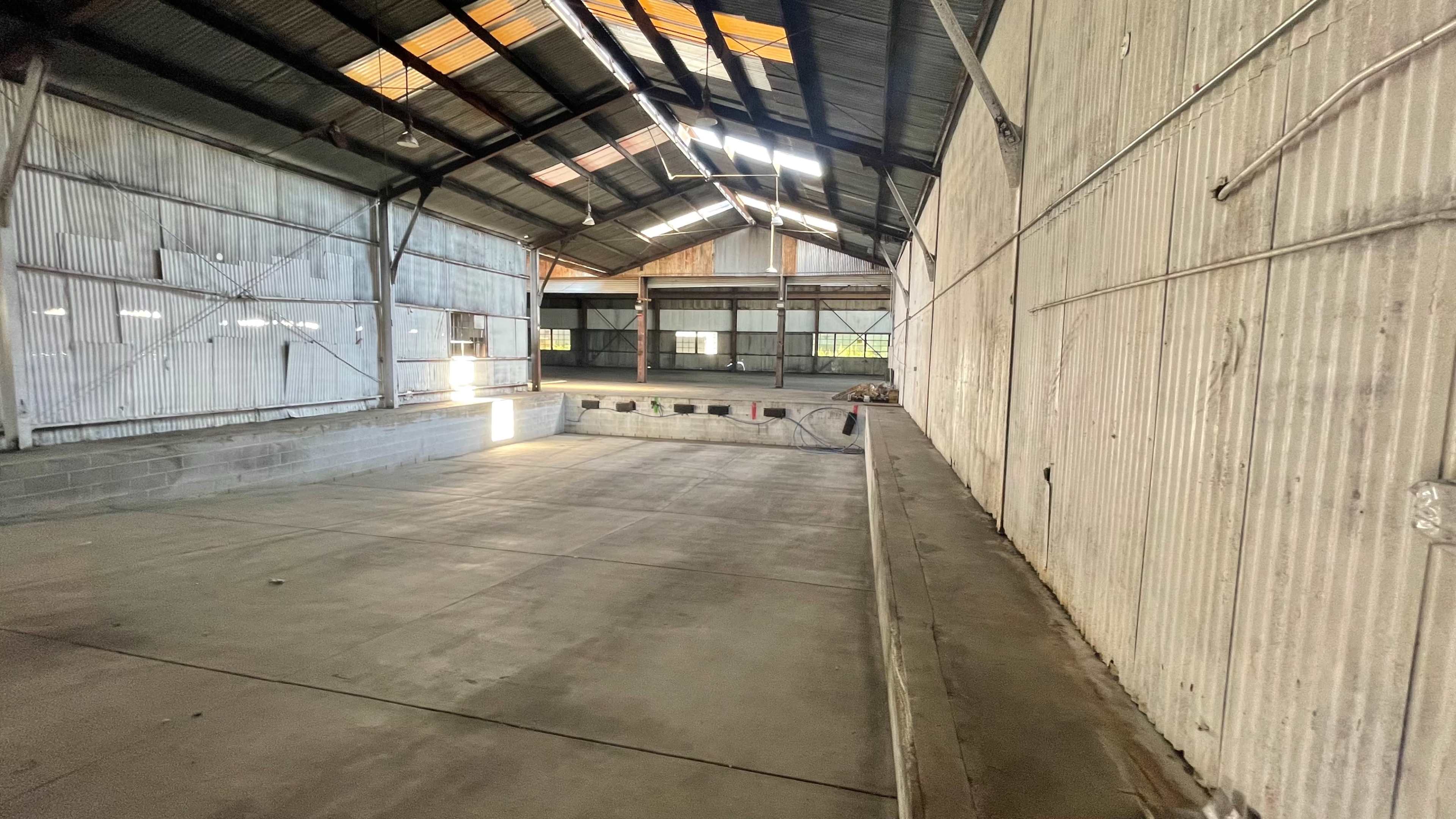 The interior of a large, vacant warehouse with metal walls, a high roof, and a concrete floor.