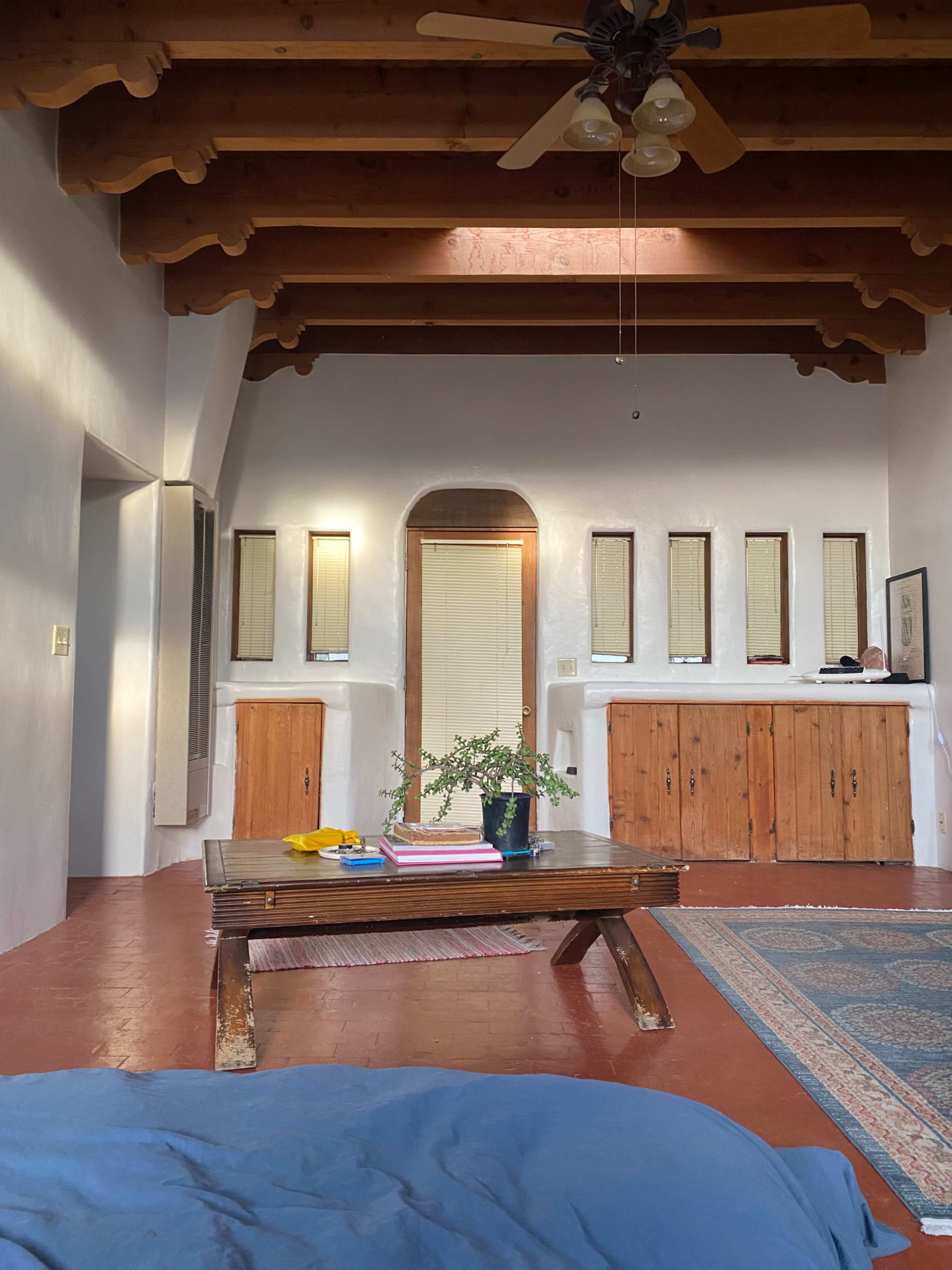 A cozy room with wooden beams, a low table in the center, and a narrow bar with several mirrors and a potted plant.