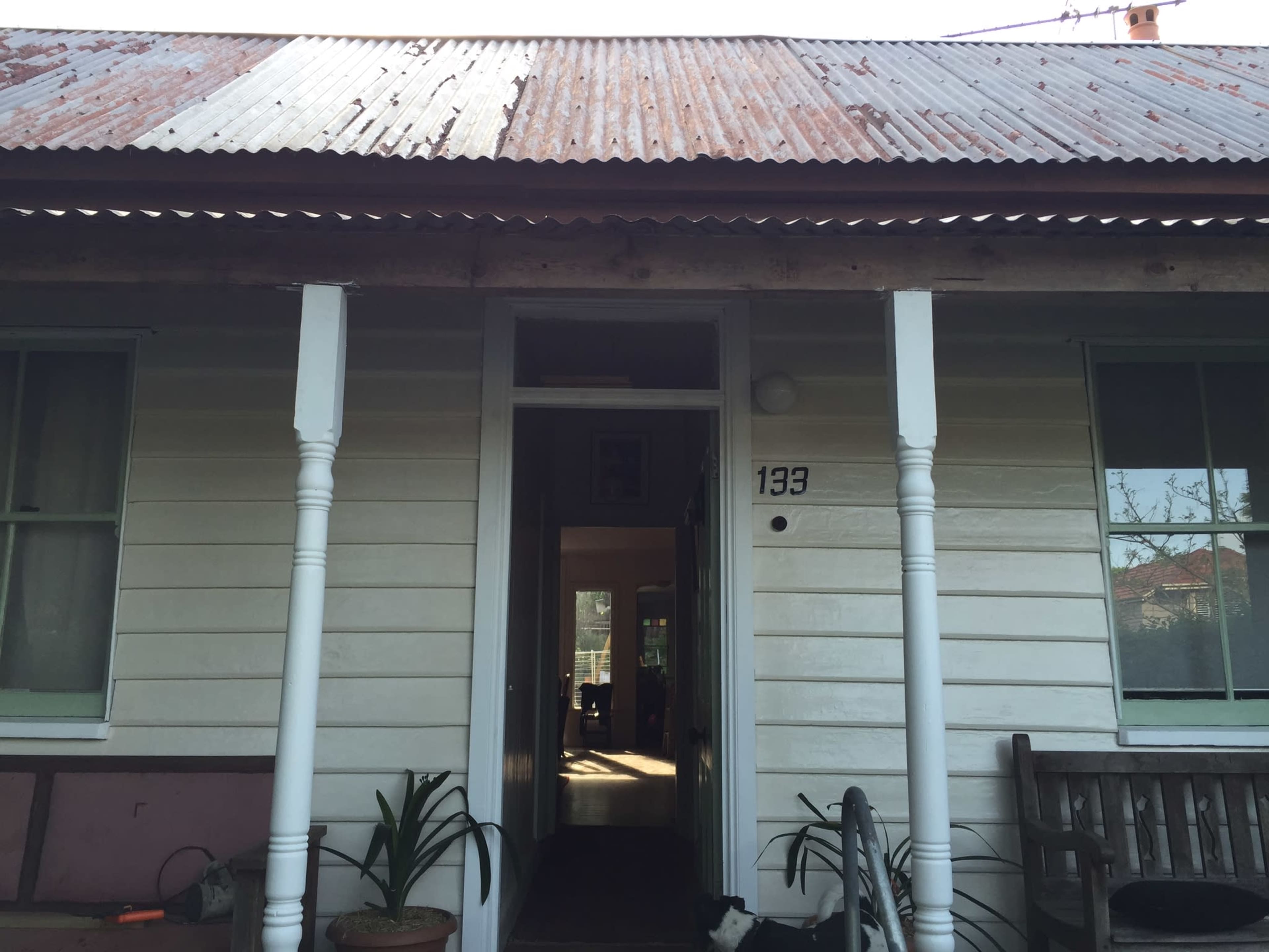 The entrance of a wooden house with a corrugated metal roof and two white pillars supporting the porch.