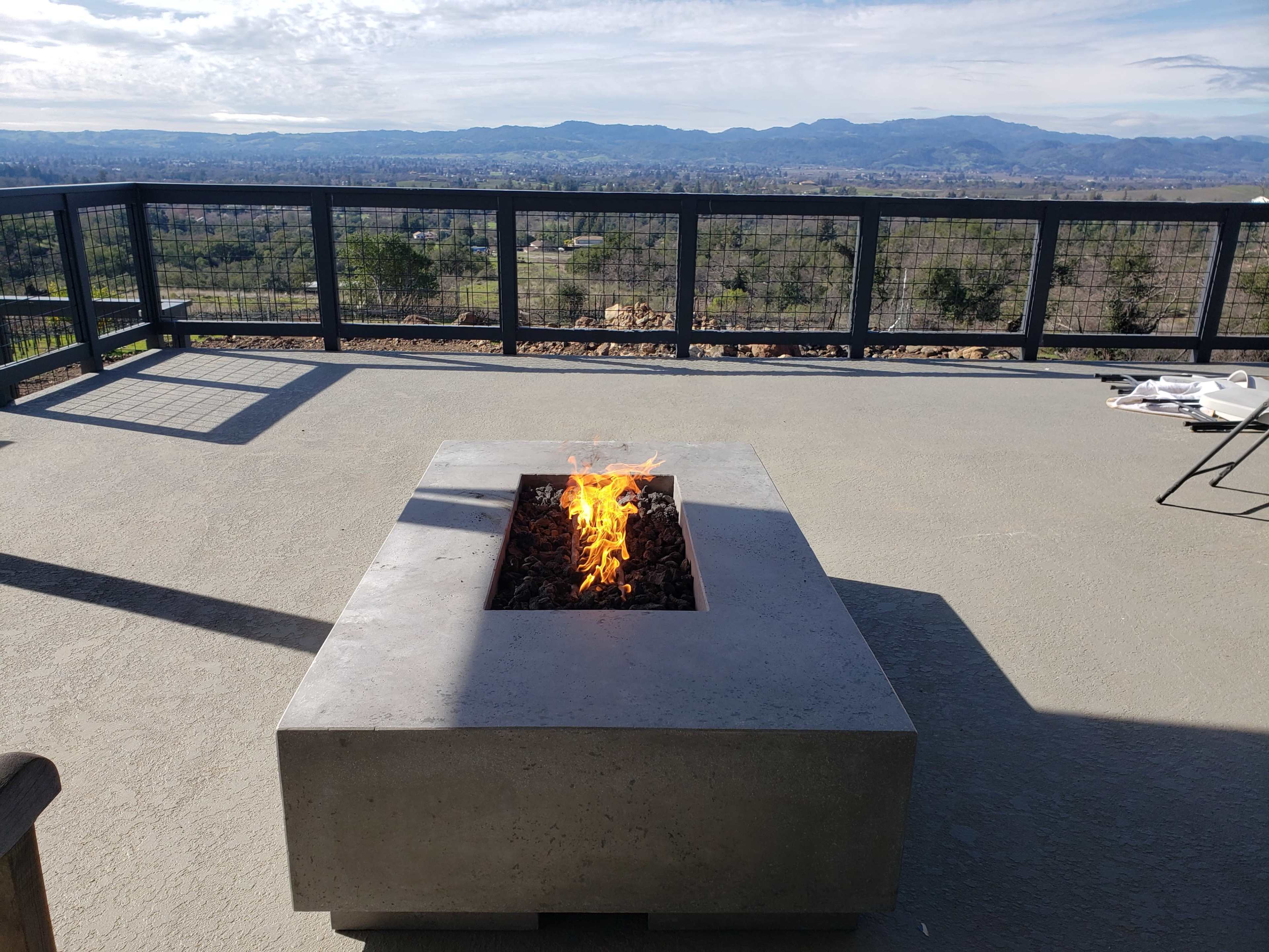 A fire pit made of concrete sits on a deck overlooking a mountainous landscape.
