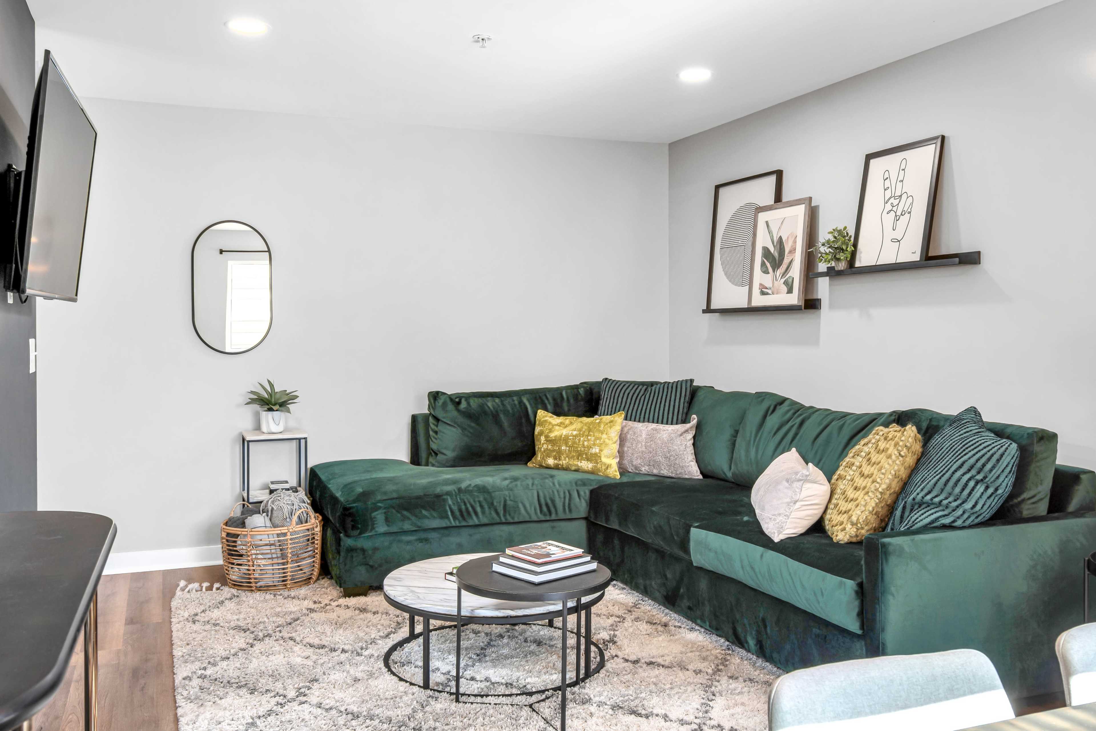 A modern living room featuring a green sectional sofa, a round coffee table, and framed artwork on the walls.