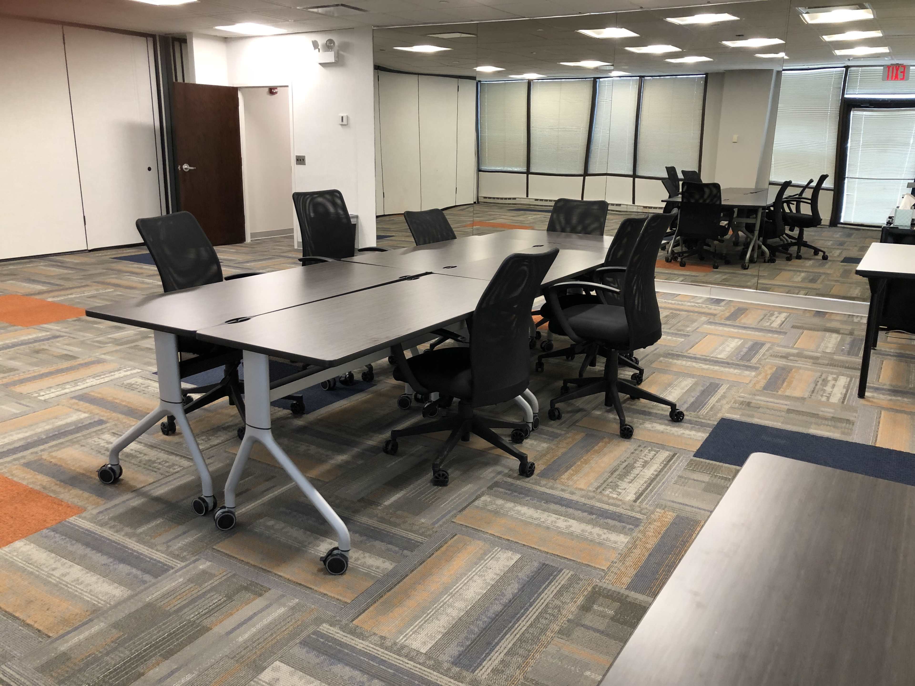 The image shows a modern office space with several movable desks and rolling chairs arranged on a patterned carpet.
