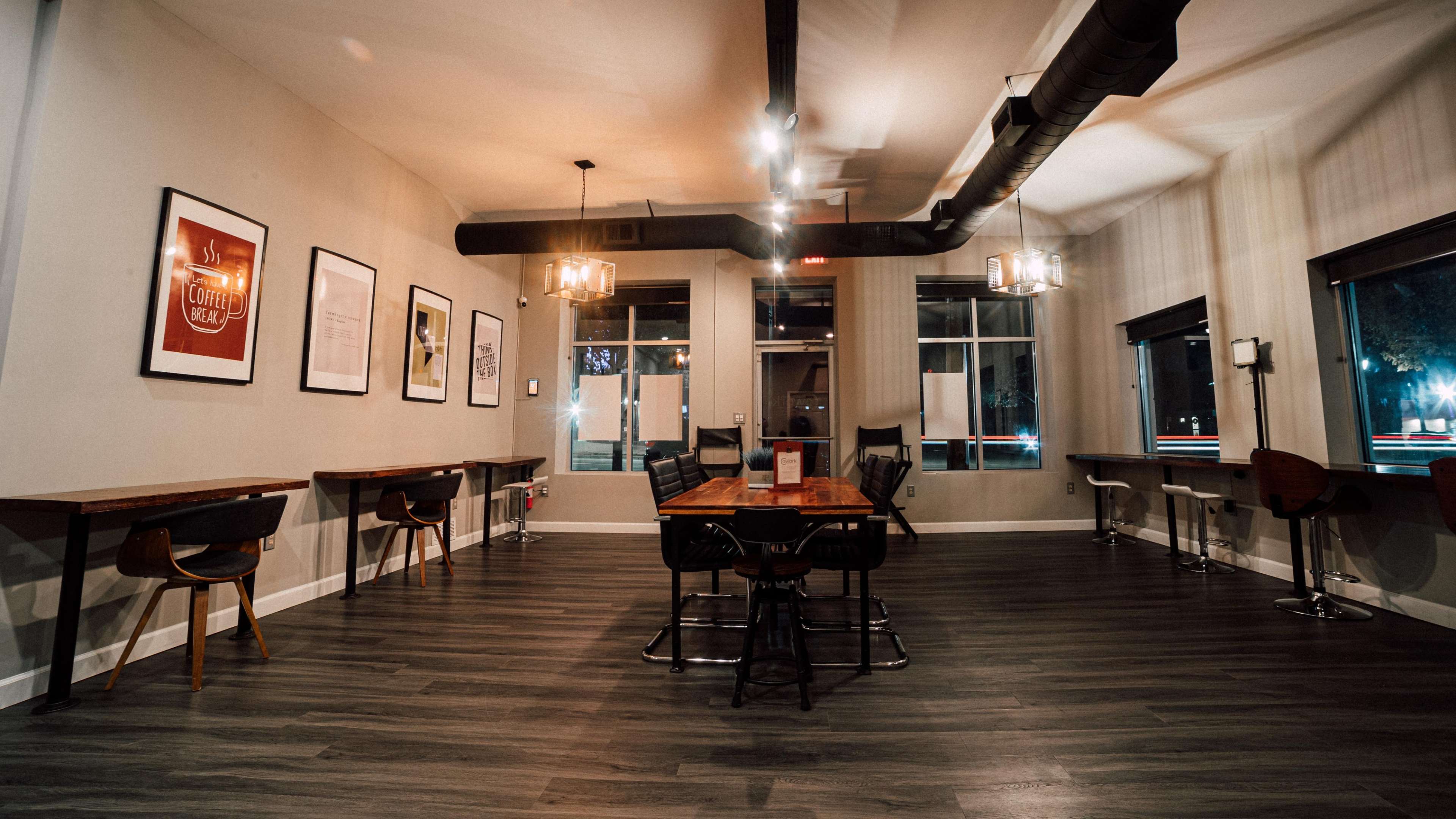 A spacious, modern cafe interior with wooden tables, black chairs, and framed artwork on the walls.