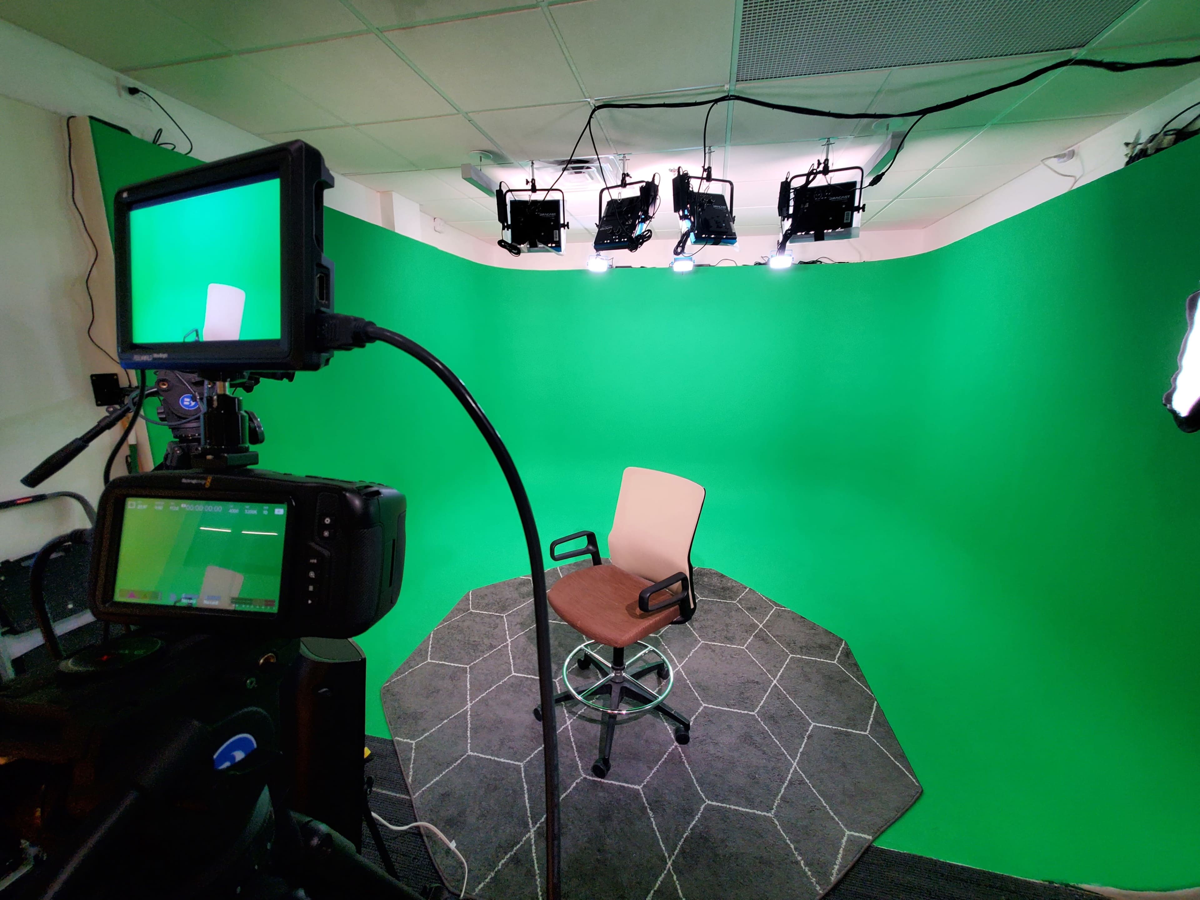 The image shows a green screen setup with a bare swivel chair in an octagonal patterned area, surrounded by multiple overhead lights.
