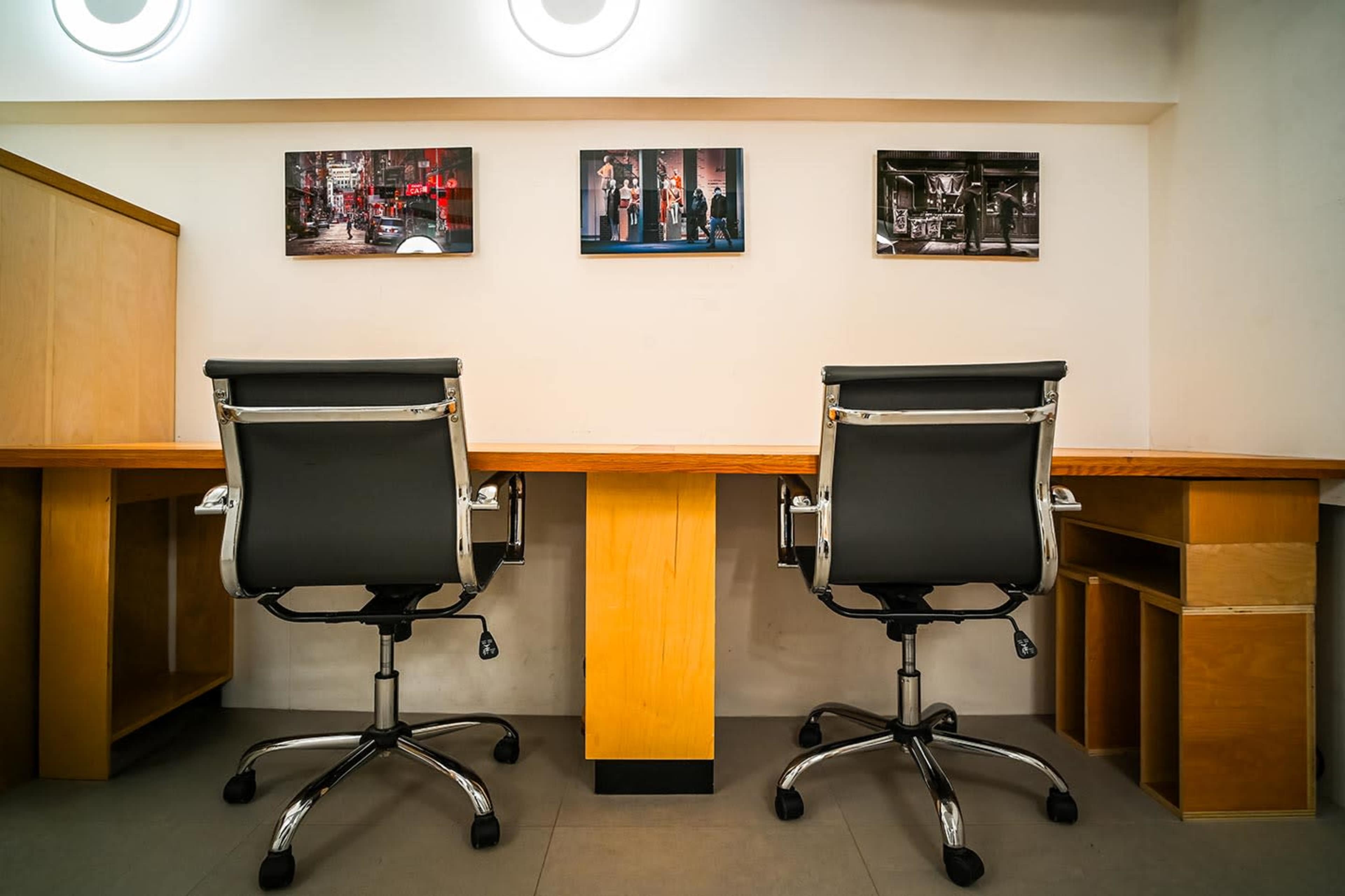 The image shows two black office chairs facing a wooden desk with three framed photographs hanging on the wall above.