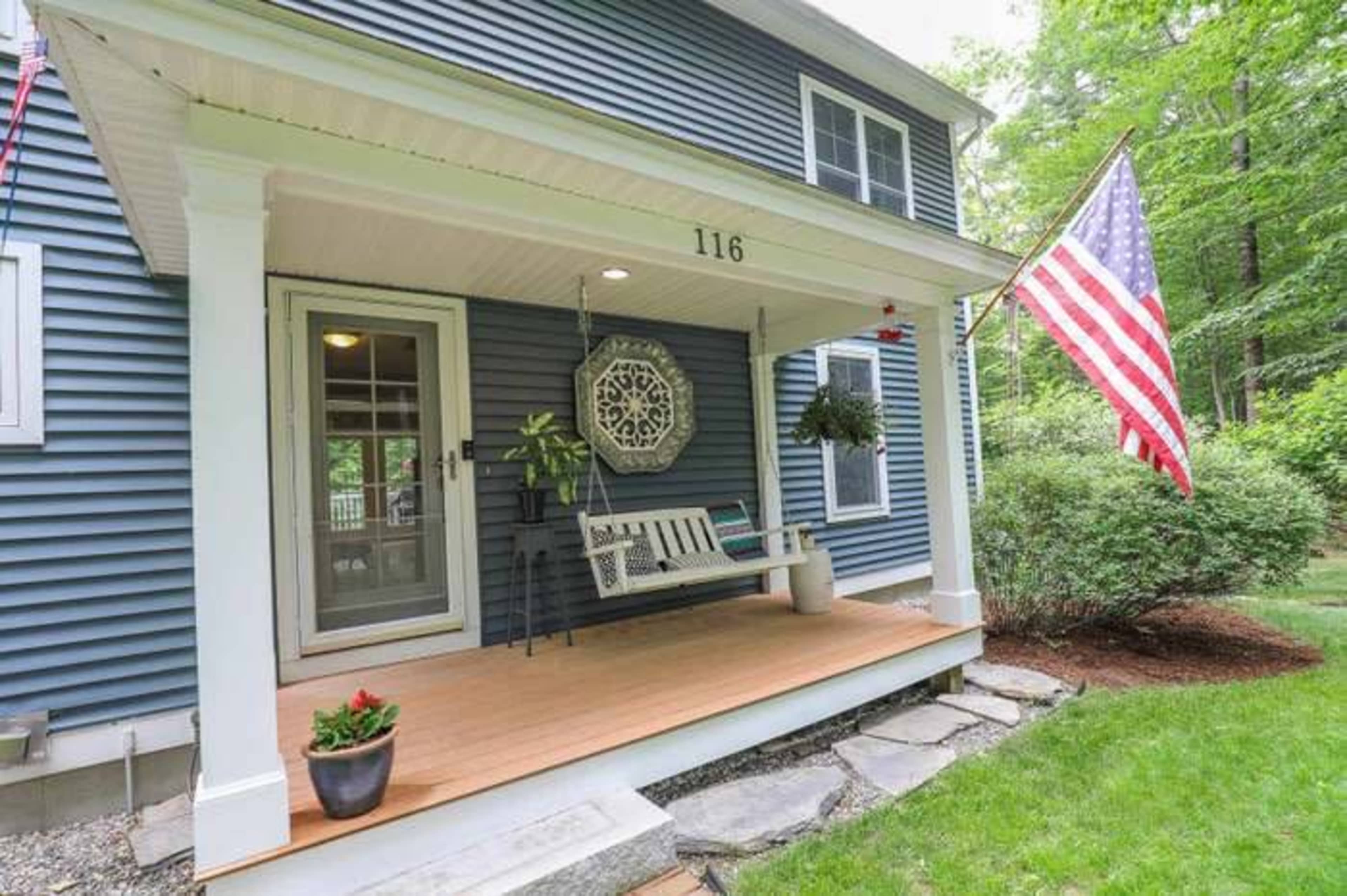 A blue house with a porch featuring a swing, an American flag, and a potted plant on the floor.