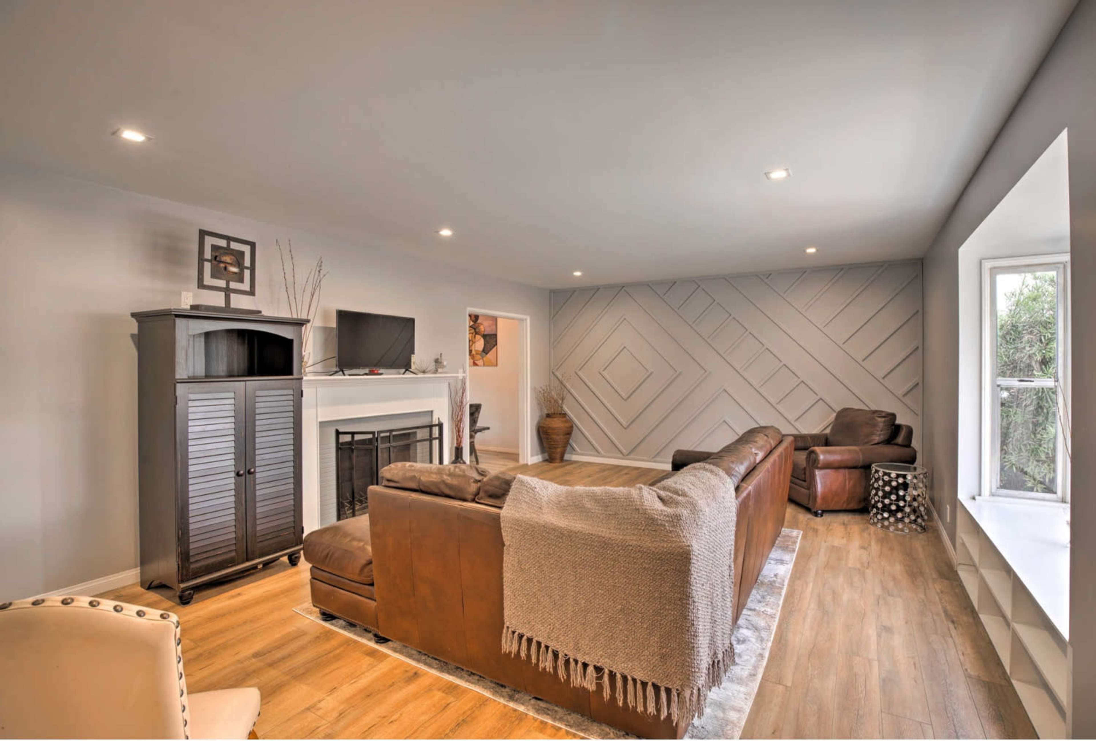 A spacious living room features a sectional sofa, a television mounted above a fireplace, and a large window with a view.
