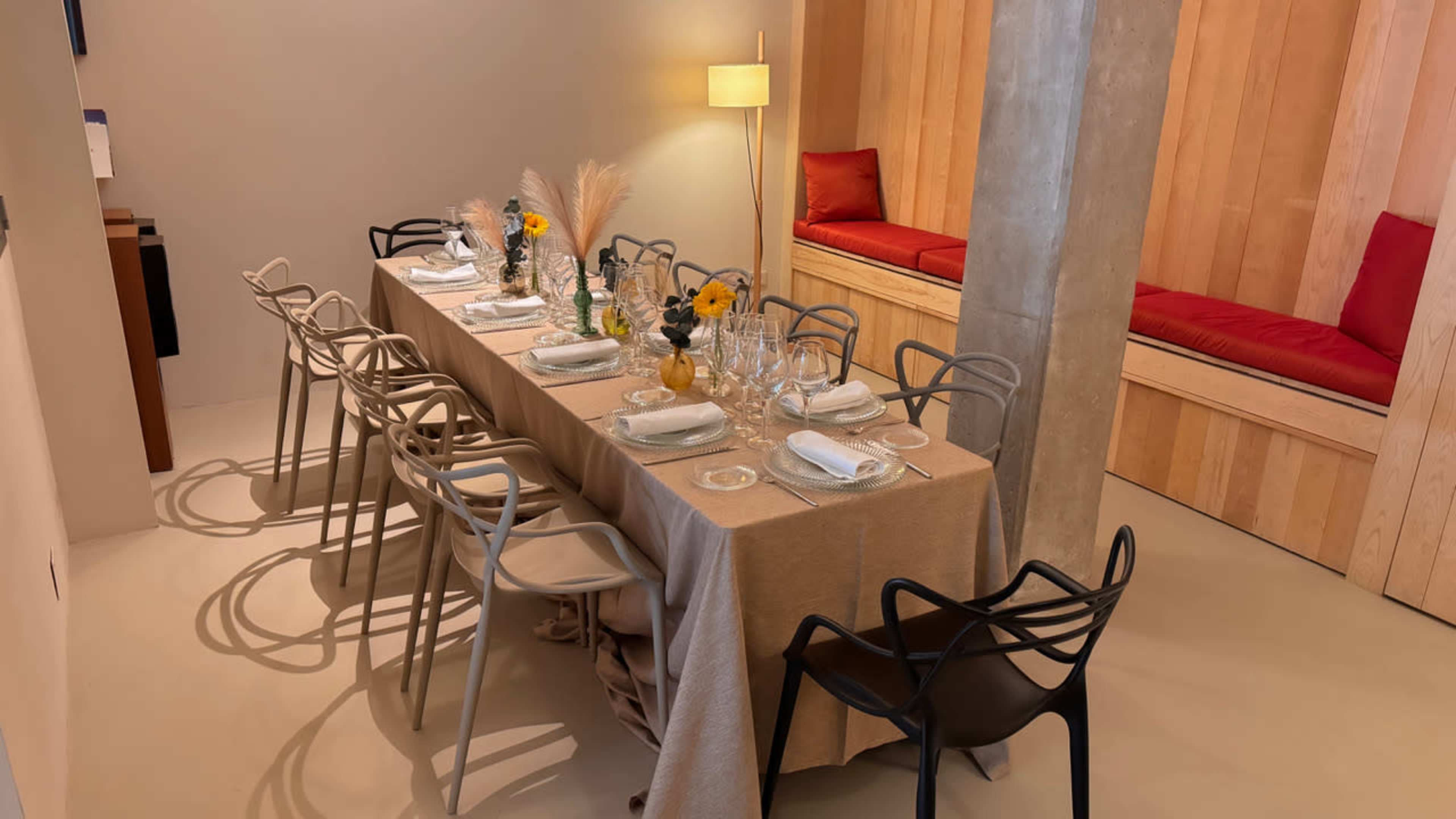 A long dining table is set with plates and glasses, surrounded by various styled chairs in a modern room with wooden accents and soft lighting.