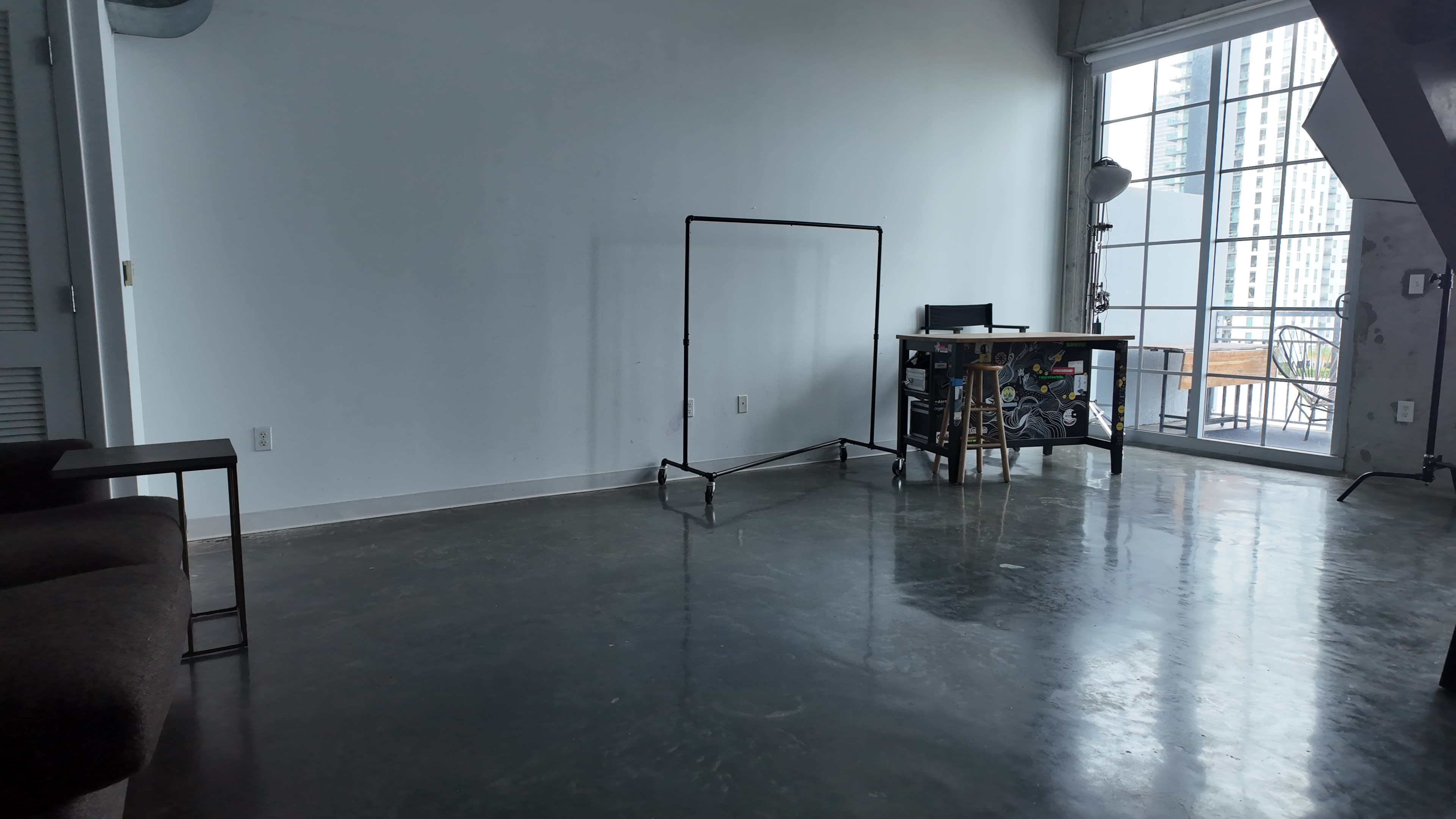 The room features a gray concrete floor with a clothing rack and a small table set against a wall of windows.