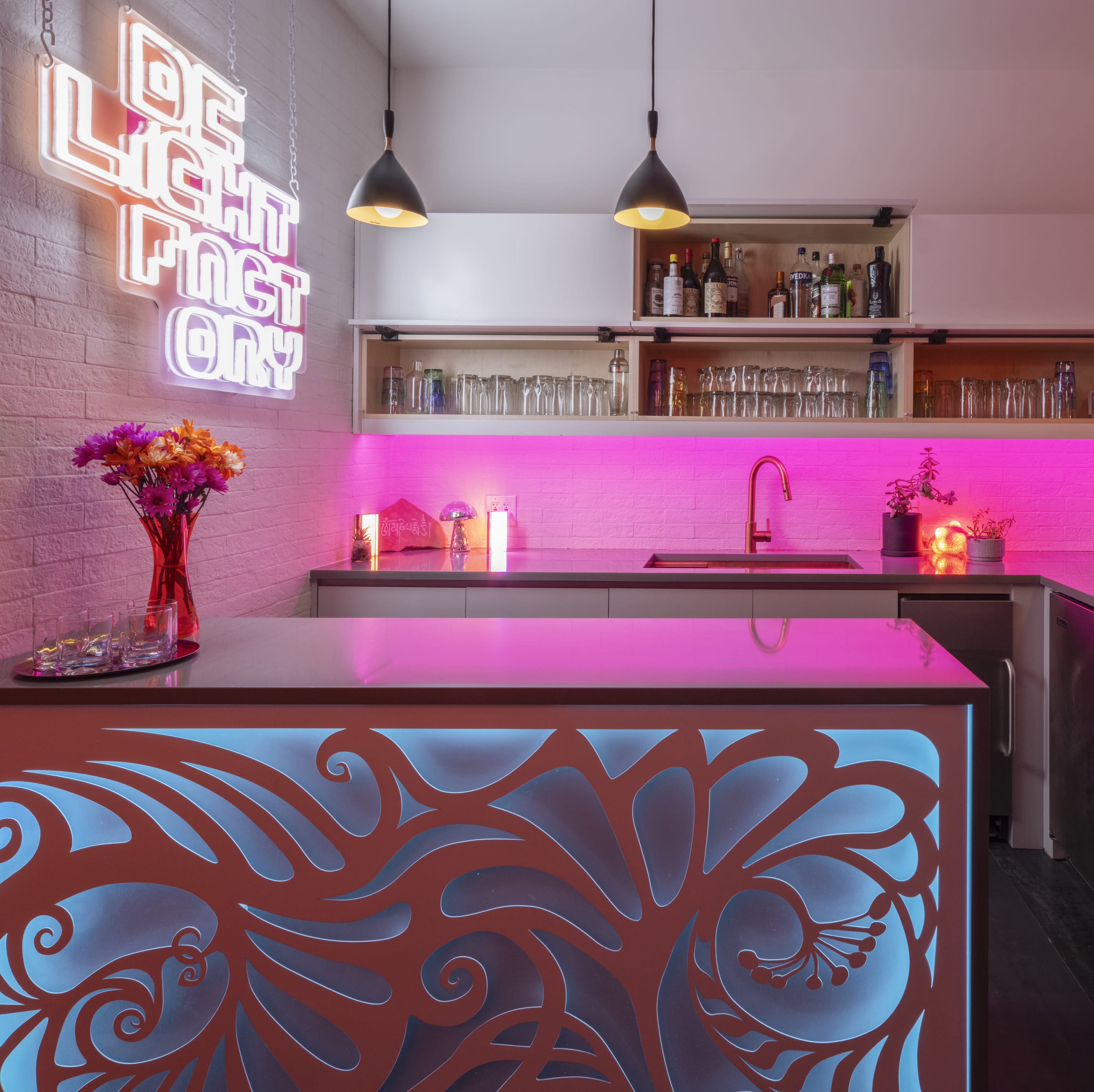 A modern kitchen features a brightly lit bar area with a decorative countertop and neon signage on the wall.