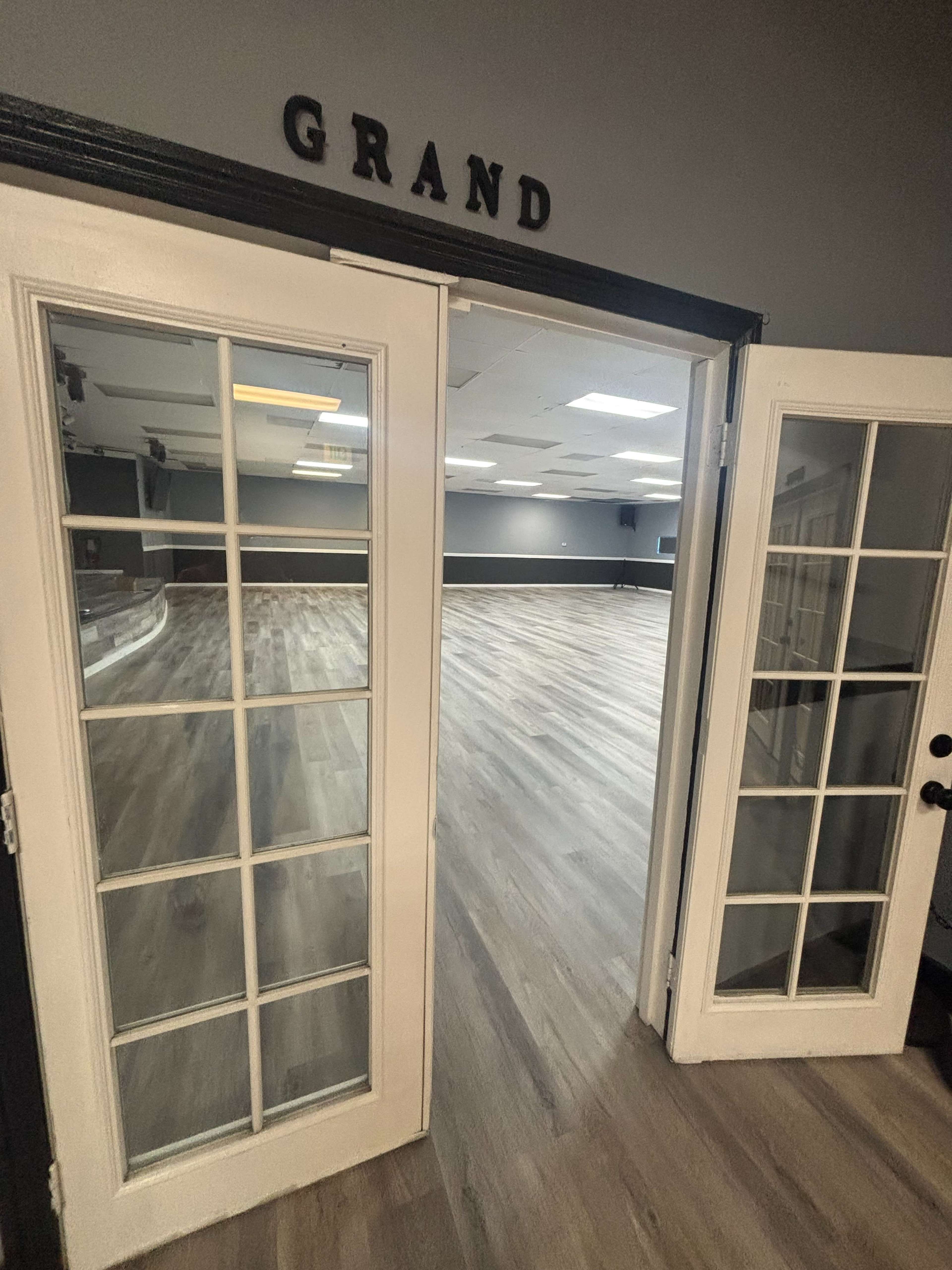 The image shows a pair of double doors opening into a spacious empty room with wooden floors and modern lighting.