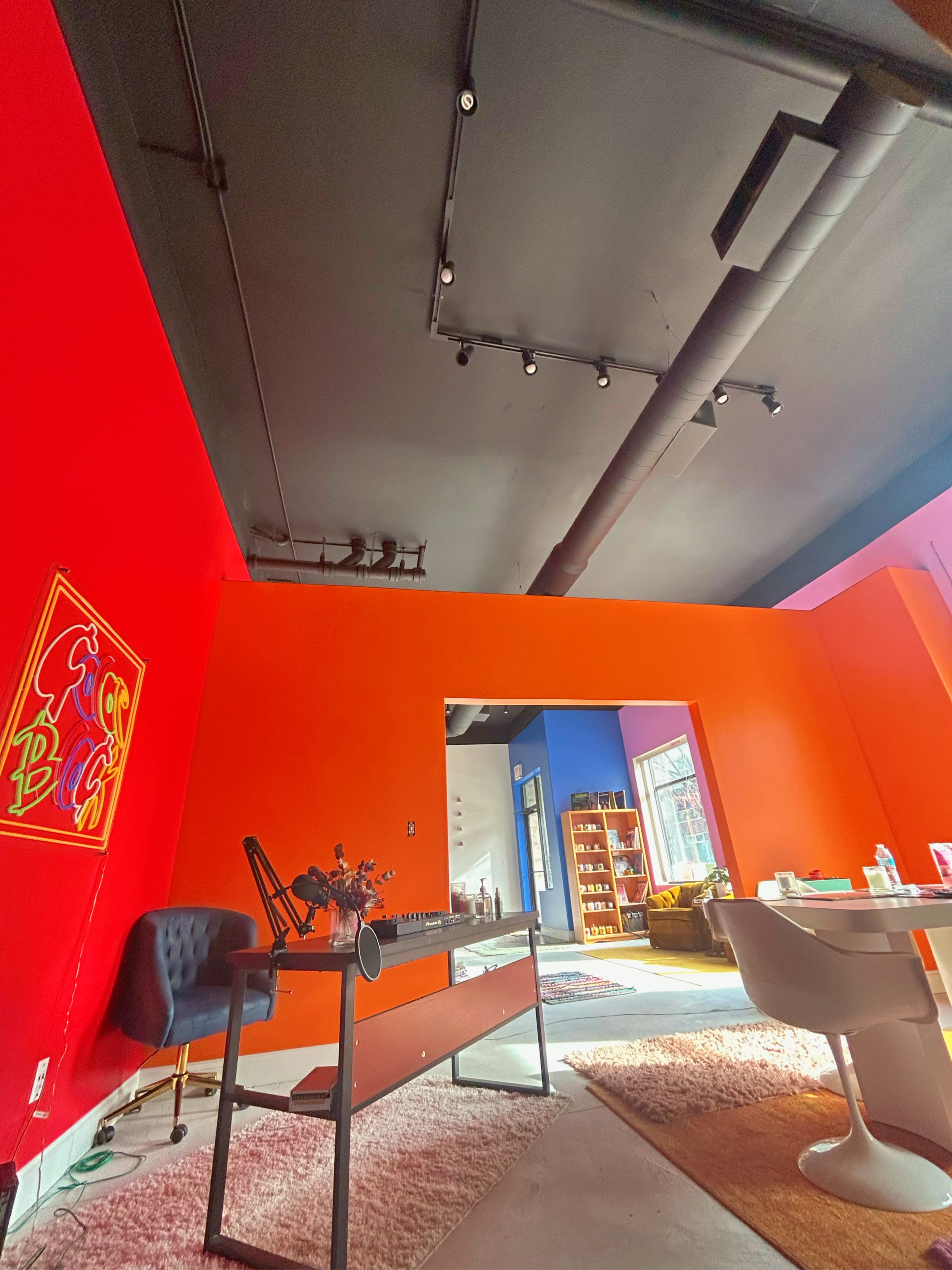 A colorful office space with red and orange walls, a desk with an office chair, and a visible room leading to a library area.