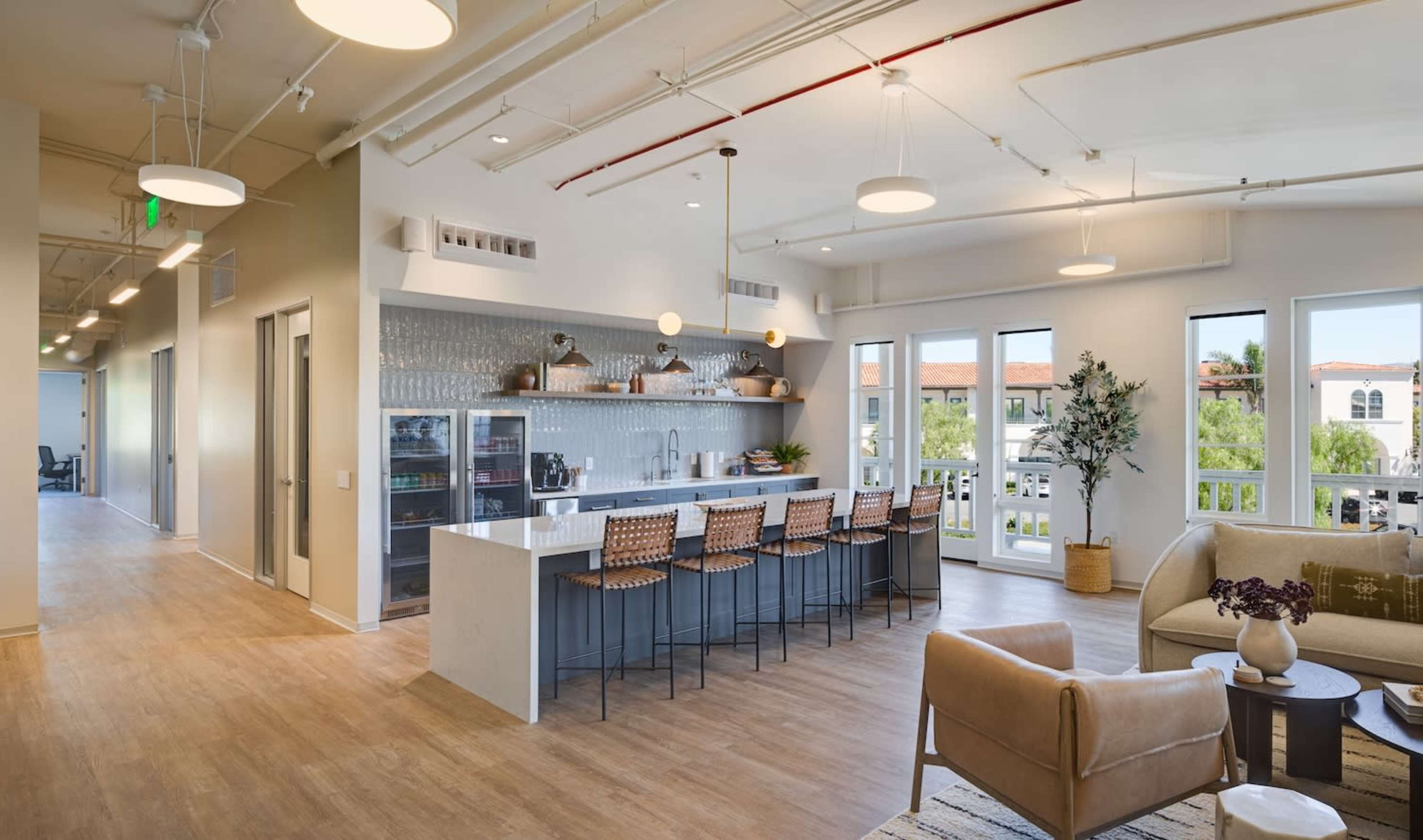 A modern kitchen area with a long countertop, high chairs, and large windows allowing natural light to illuminate the space.